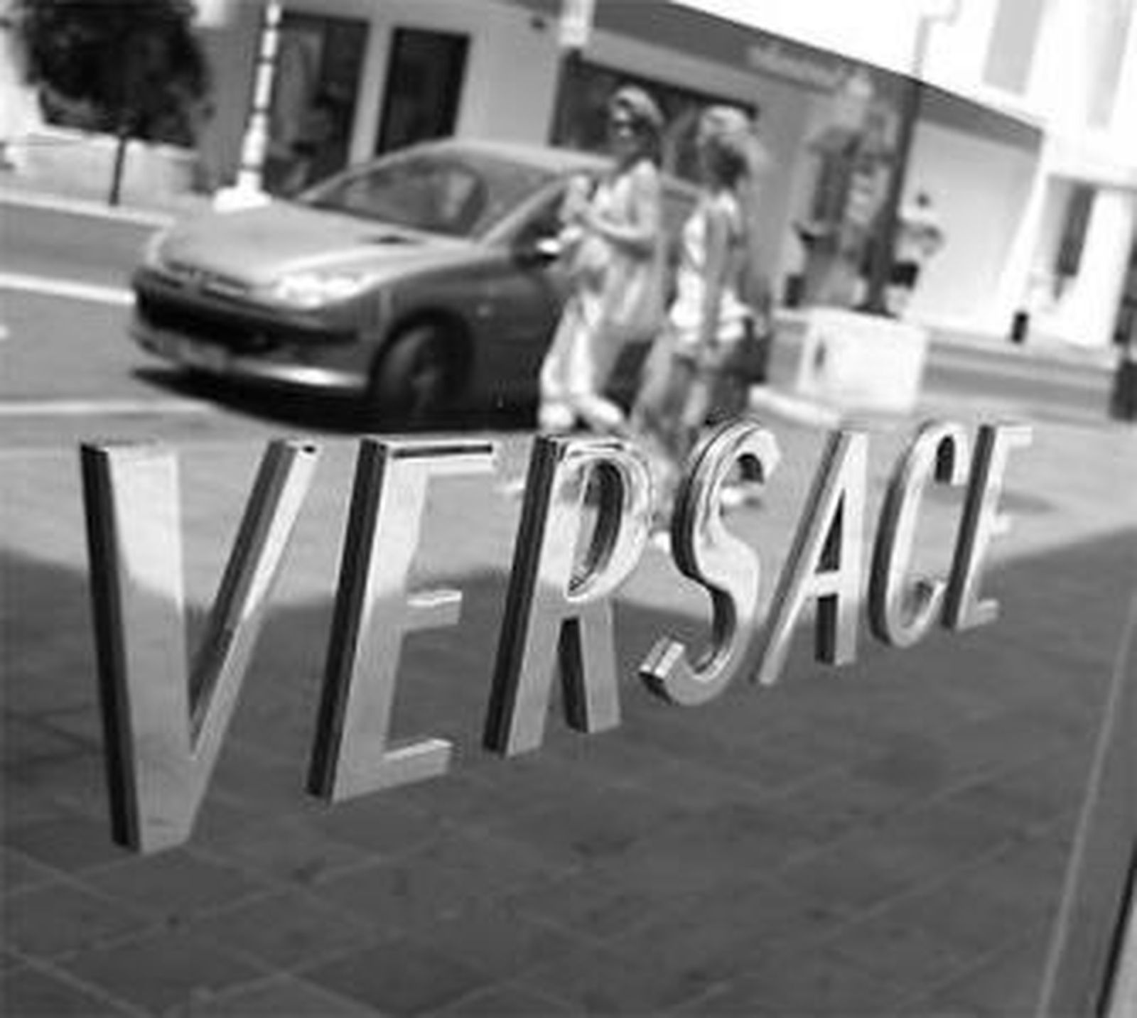 Dos mujeres se reflejan en el cartel de Versace en Puerto Banús.