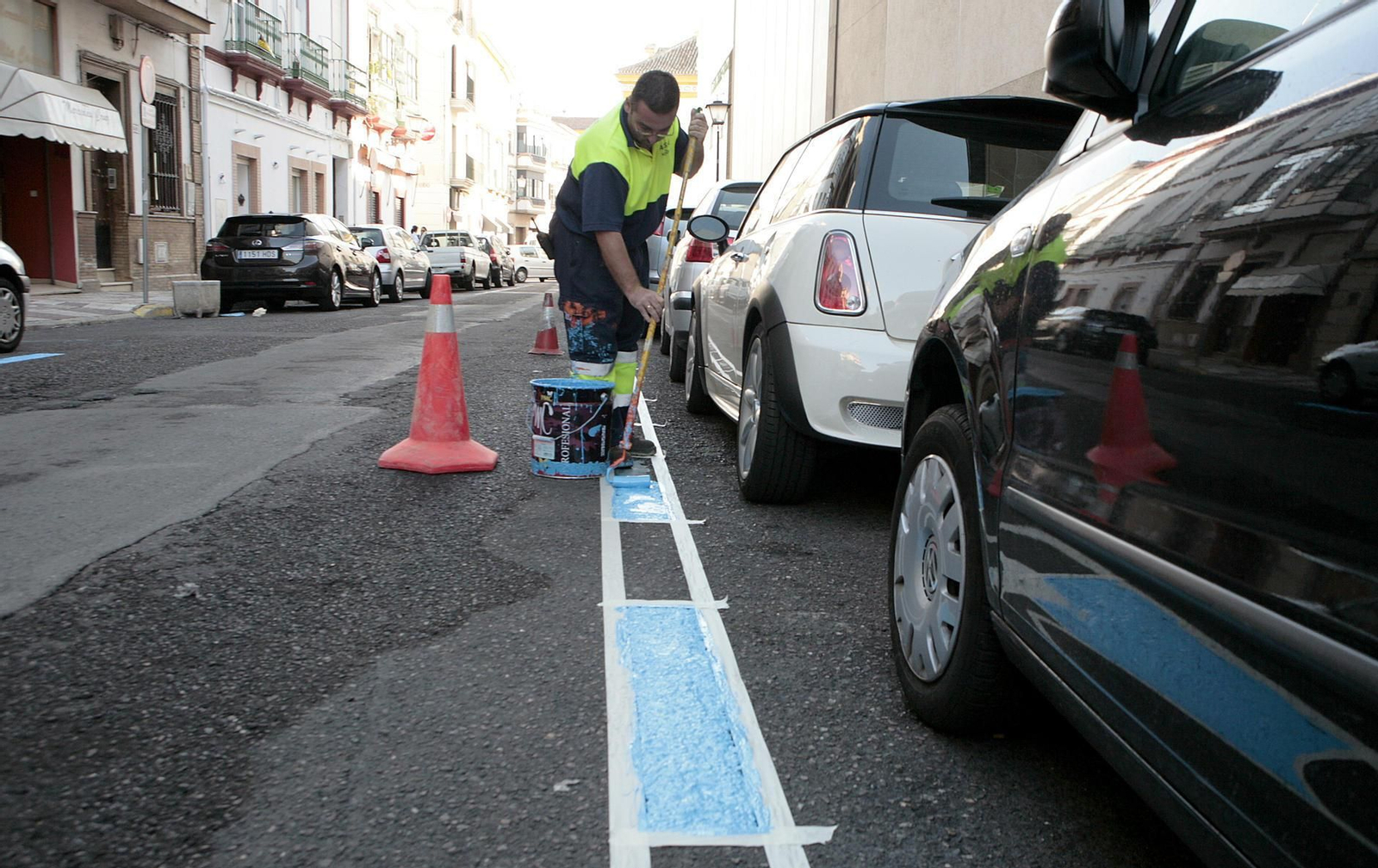 Imagen de archivo de un operario pintando una línea azul de aparcamiento.