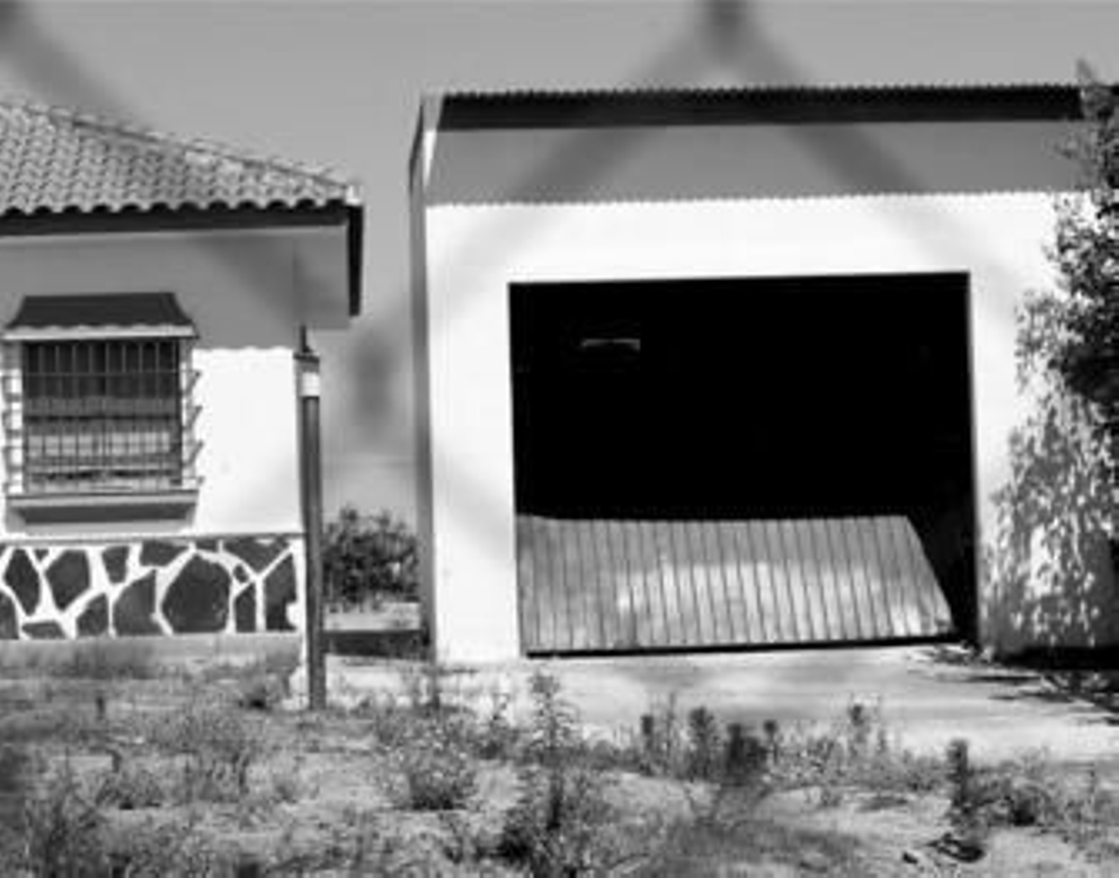 Vista del chalé (izquierda) y del garaje en el que estaba secuestrado Rafael Ávila en Almonte. Como se ve, la puerta fue reventada por los GEO.