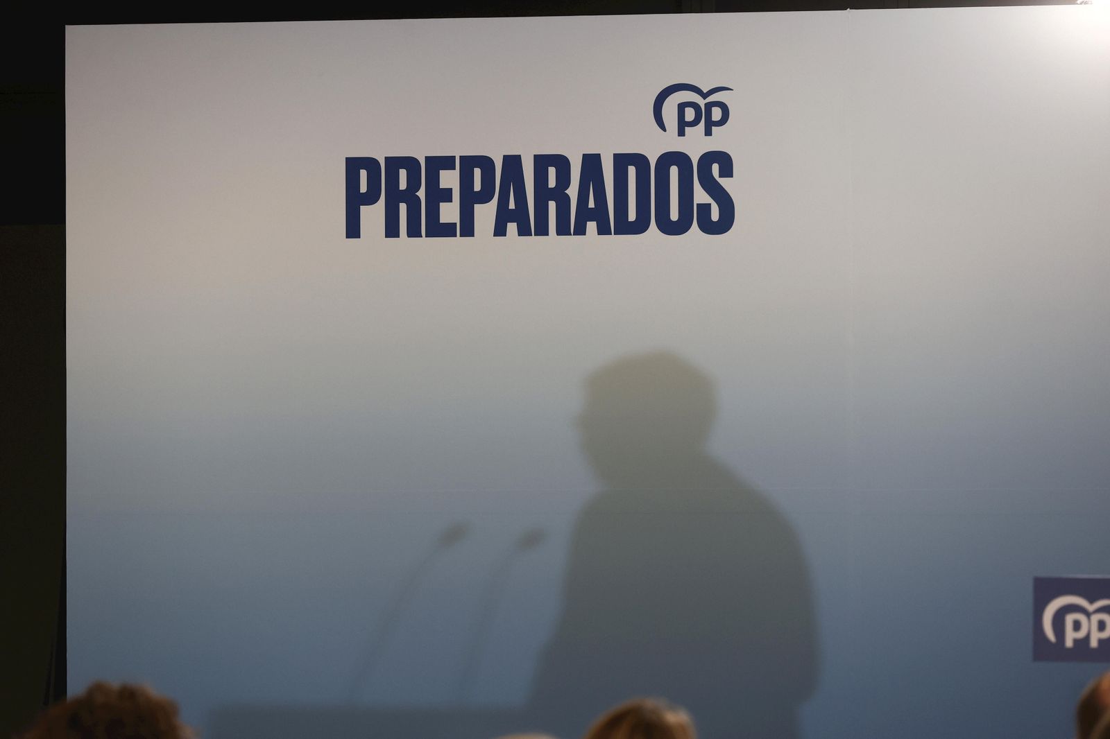 La sombra de Núñez Feijóo se proyecta en un panel del PP en un mitin.