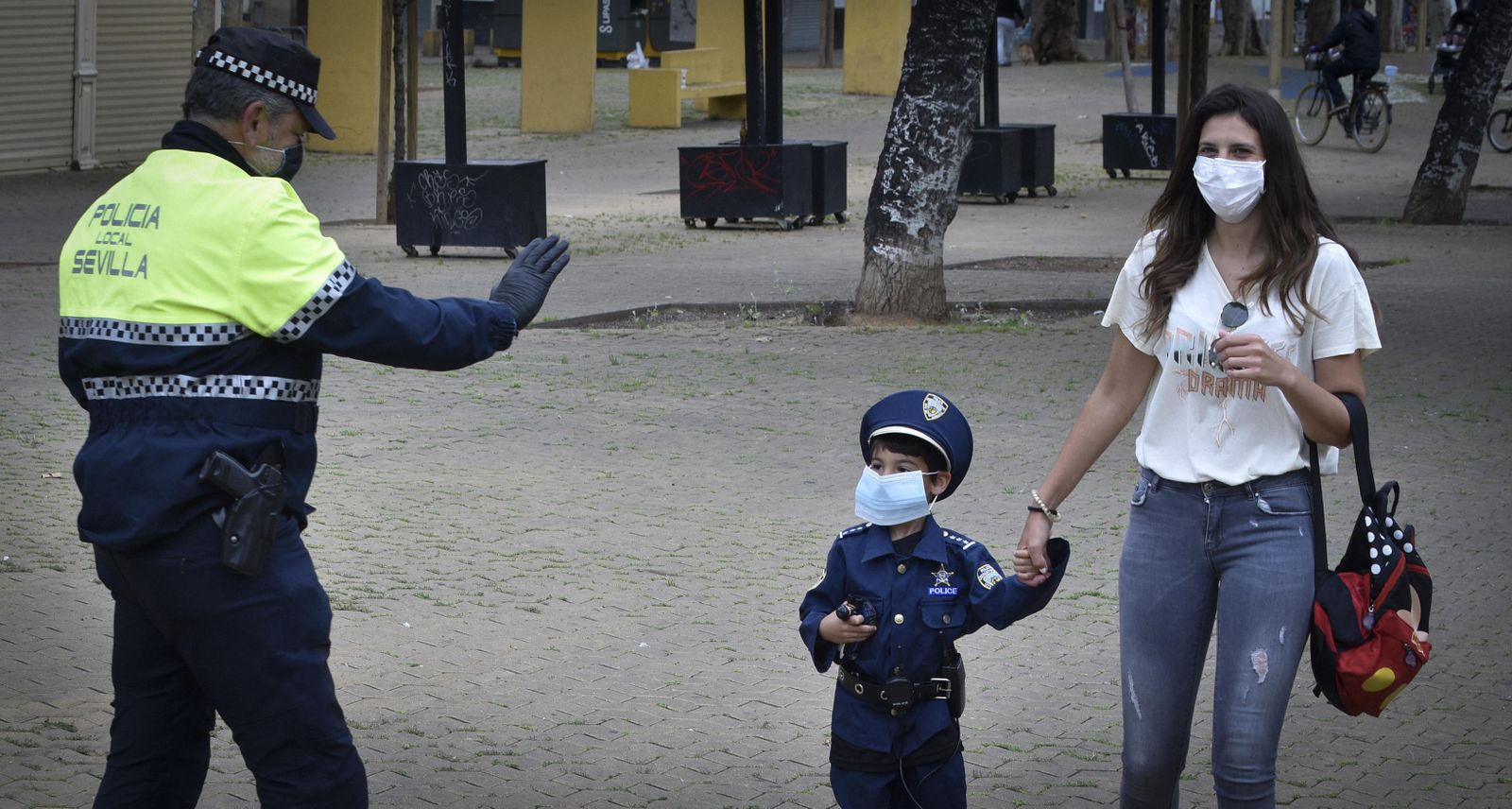 Un agente saluda a un niño vestido con el uniforme policial tras regalarle una mascarilla.