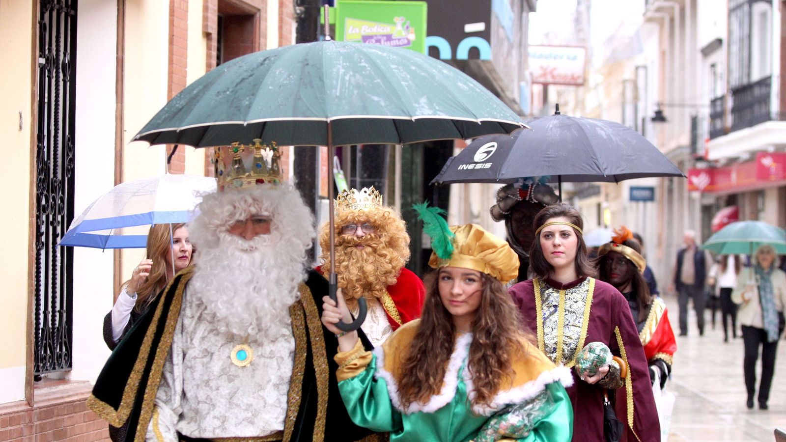 Los Reyes Magos se protegen de la llucia por las calles de Huelva.