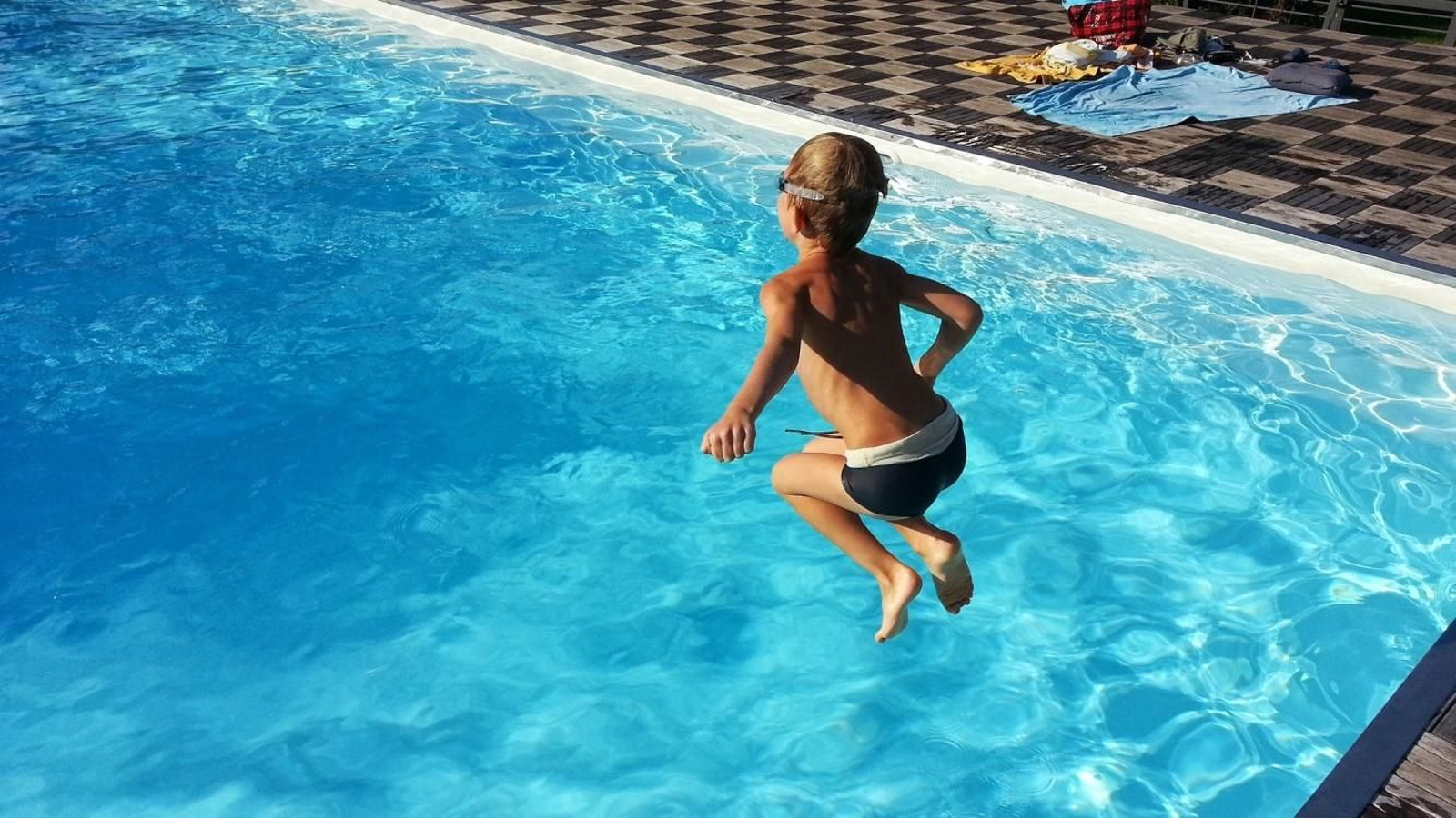 Un niño tirándose a la piscina con gafas de natación.