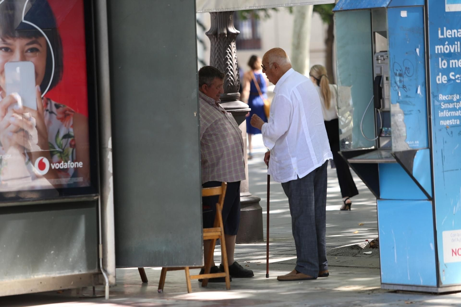 Una persona mayor conversa con un quiosquero.