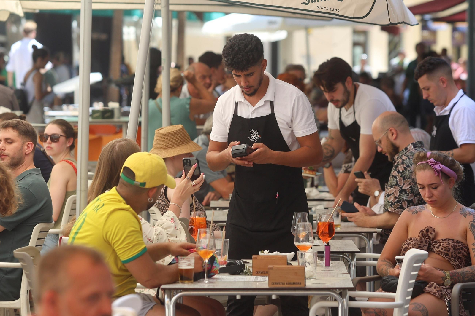 Varios camareros atienden a los clientes en una terraza de bar en Málaga.
