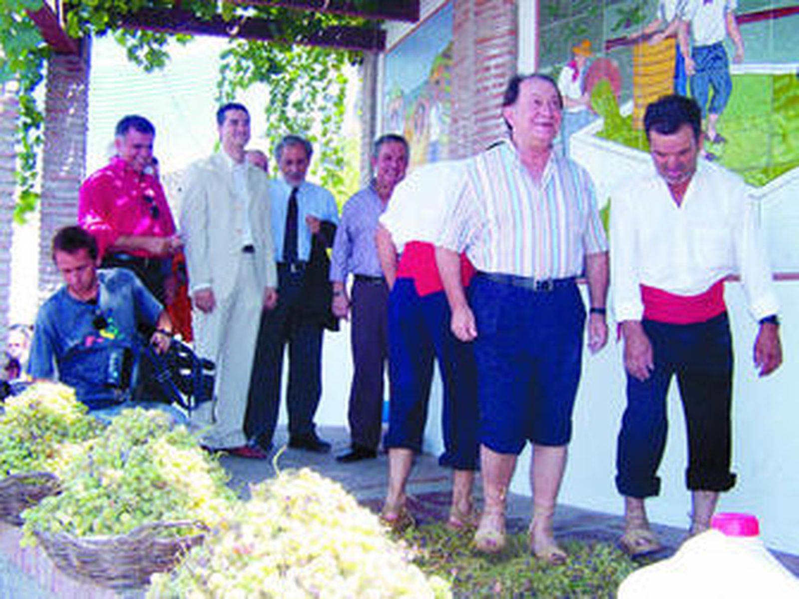 Jesús Mora, en primer plano, pisa las uvas con el alcalde detrás.