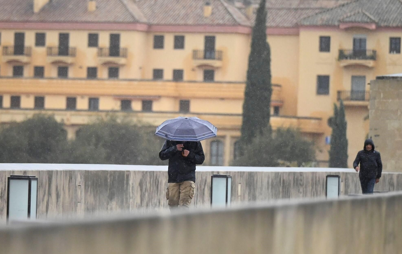 Varias personas caminan bajo la lluvia por el Puente Romano de Córdoba