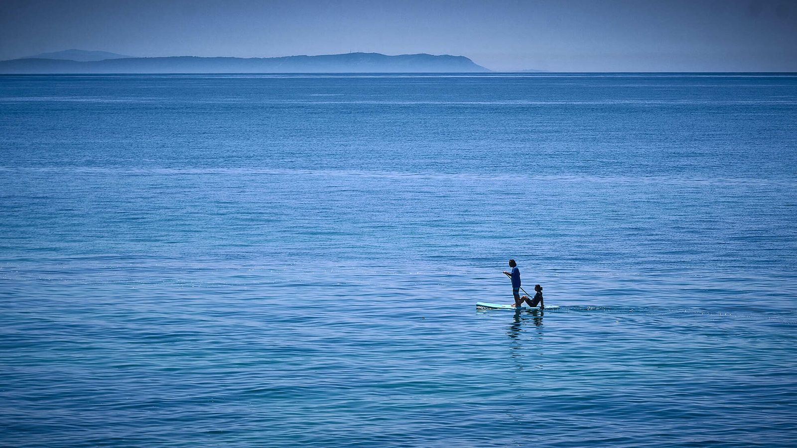 Playas de Barbate. Una pareja navega en una tabla de Paddle Surf frente a la costa de Barbate. Al fondo el cabo Espartel, ya en continente africano.