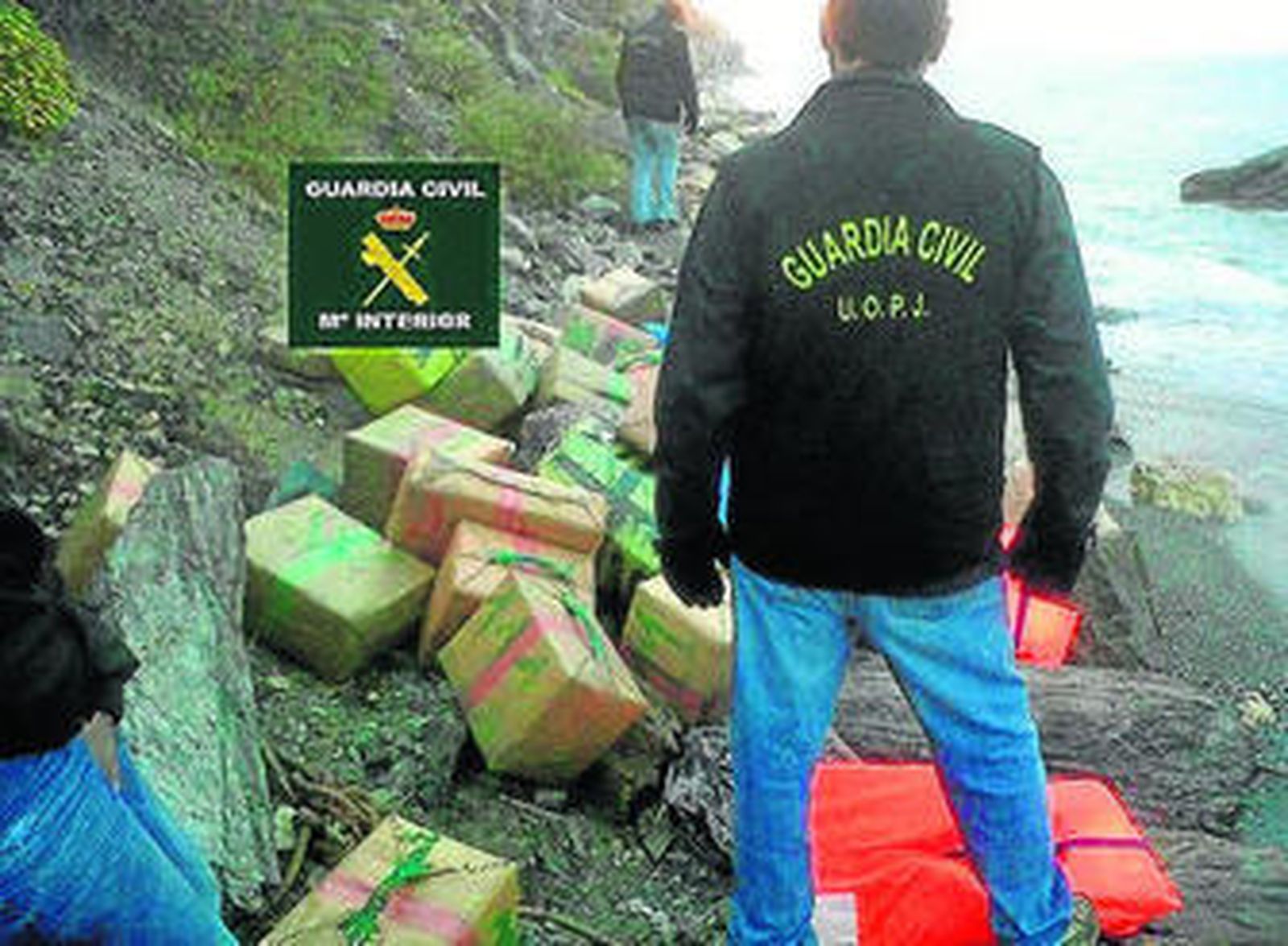 1. Un investigador de  la Guardia Civil observa  los alijos en la playa de Almayate. 2. Otro agente derriba una pared en la
