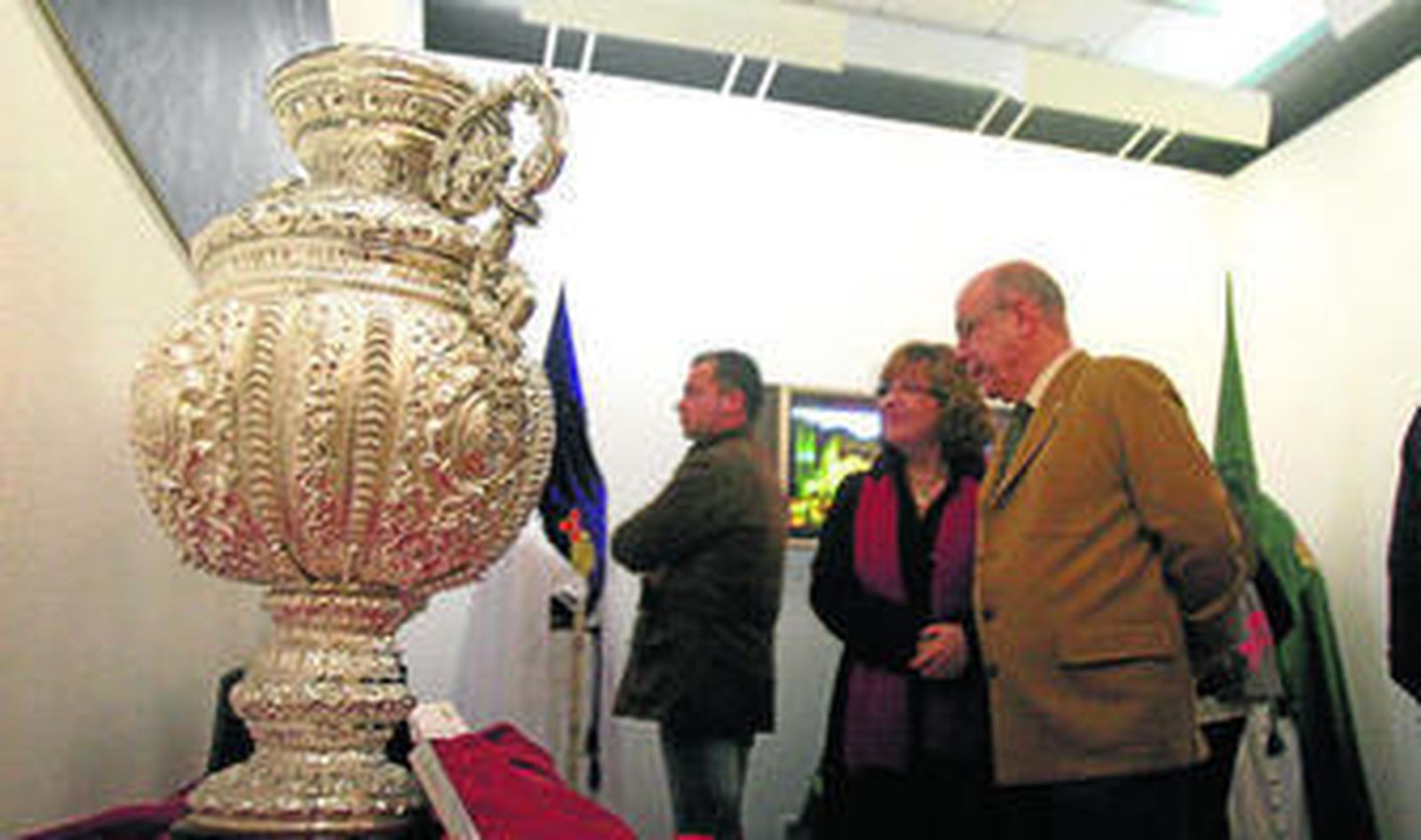 1. Los enseres de la Hermandad de San Francisco se pueden ver en la Casa Colón, como esta jarra con el escudo del Recreativo. 2. El alcalde de Huelva acompañado por el teniente alcalde de Cultura, hermano mayor de la Esperanza, el presidente del Consejo, el comandante de Marina y el diseñador de la exposición, ante una foto de la coronación. 3. Una fotografía de un altar de cultos con los candeleros 4. Foto y la misma saya. 5. Preseas de la coronación.