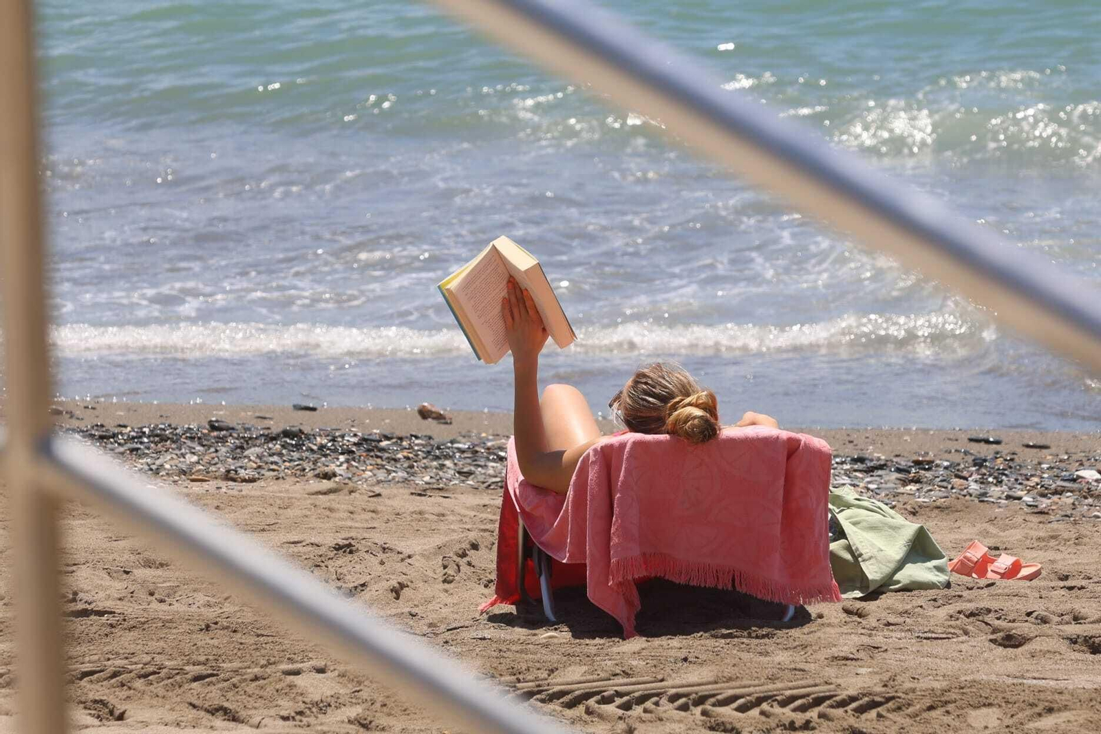 Una mujer leyendo un libro mientras toma el sol en una playa de Málaga.