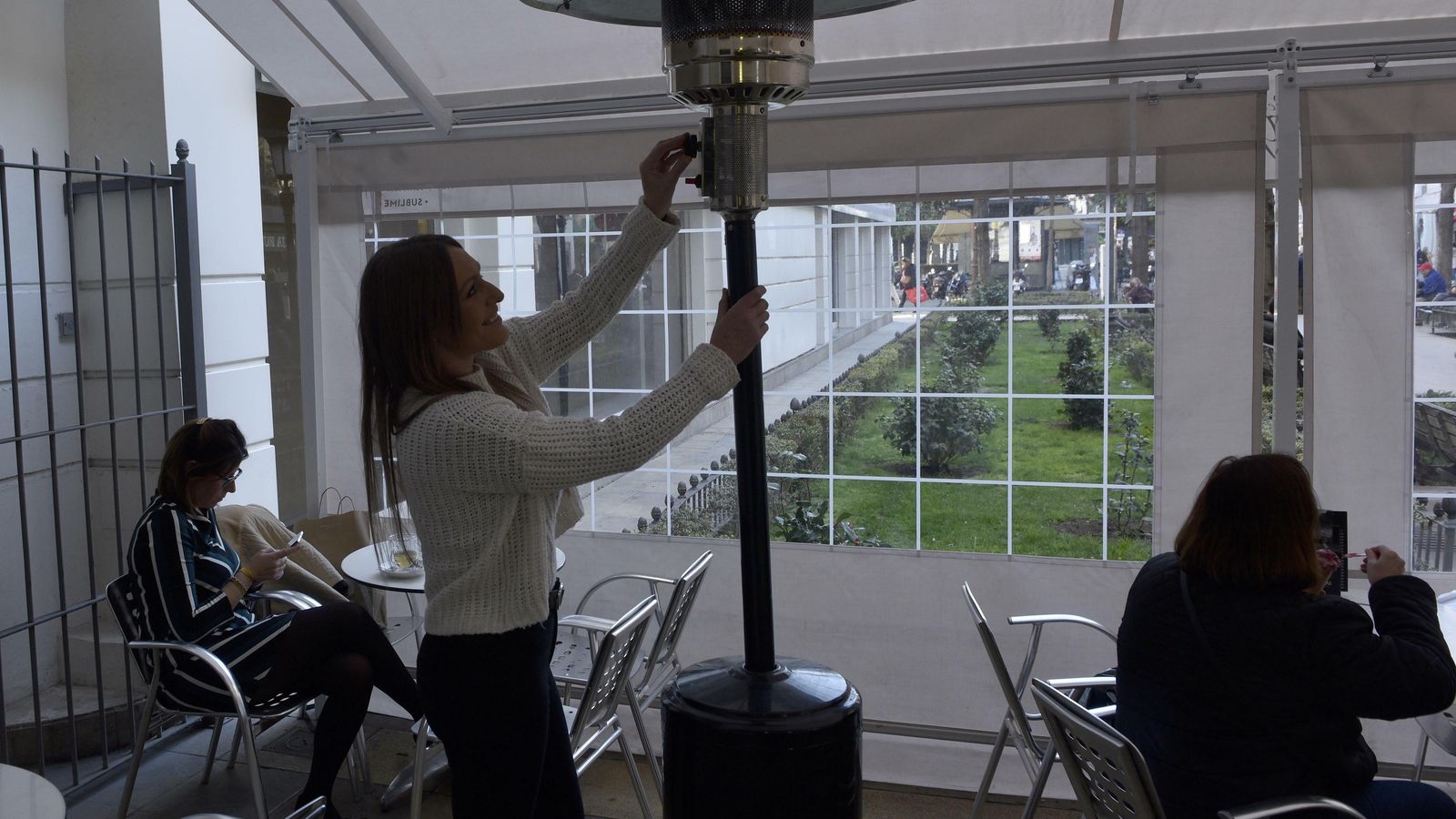 La empleada de un bar se dispone a encender un 'seta' calefactoras en una terraza.