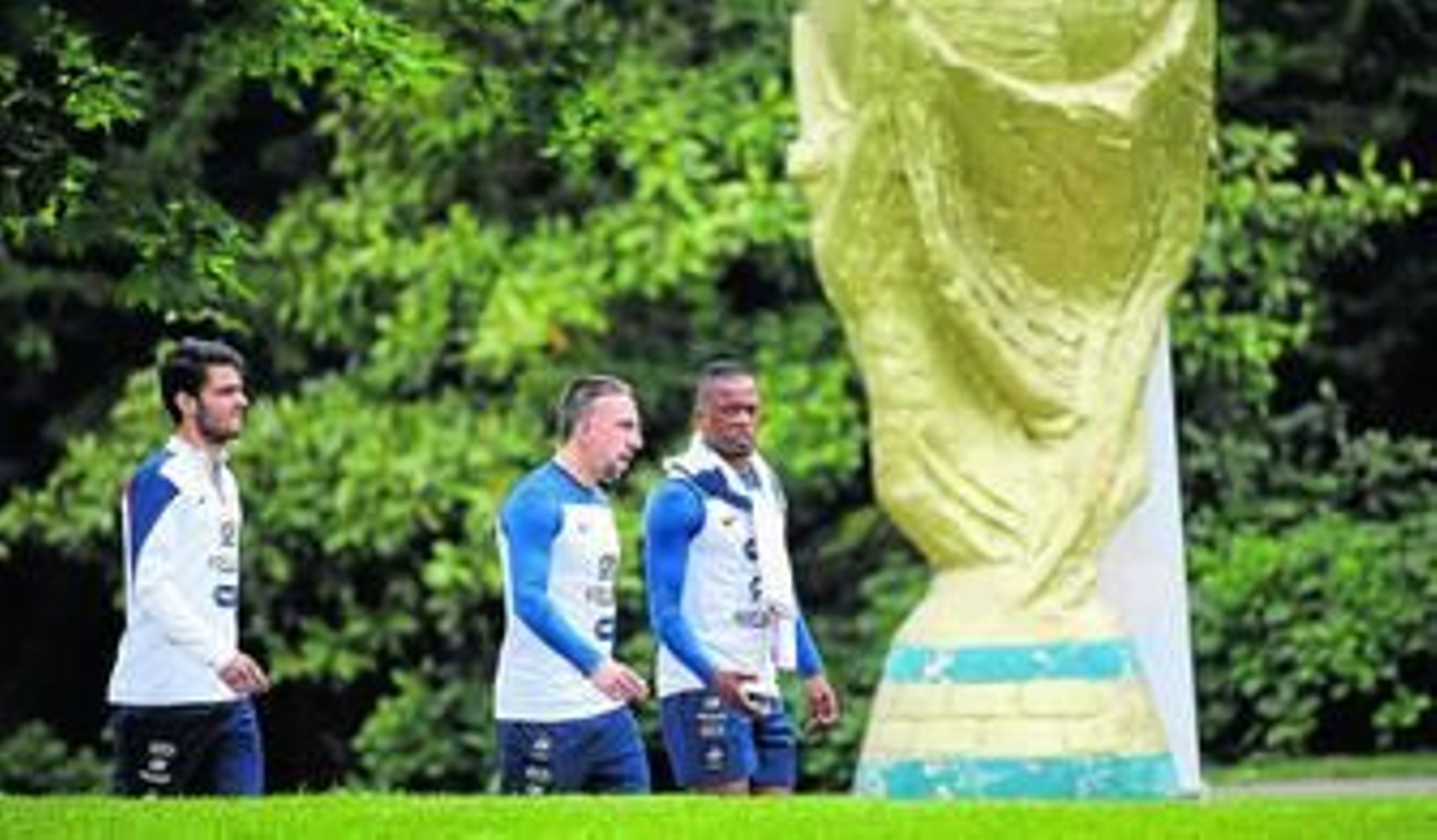 Clement Grenier, Franck Ribery y Patrice Evra pasean con una escultura de la Copa del Mundo en primer plano.