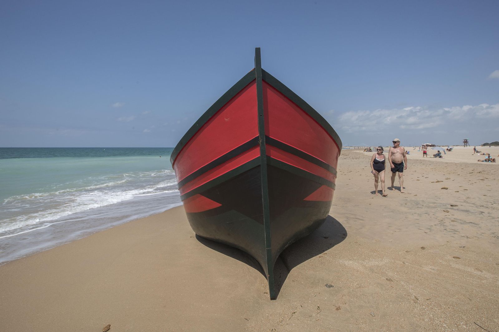 Bañistas observan la patera mientras pasan por su lado.