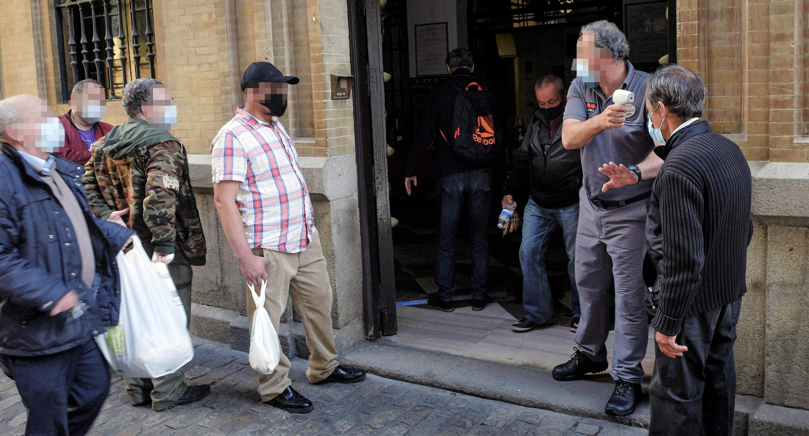 Un vigilante toma la temperatura a un usuario del comedor y centro social de la Orden de San Juan de Dios, junto a las setas, mientras otros esperan.