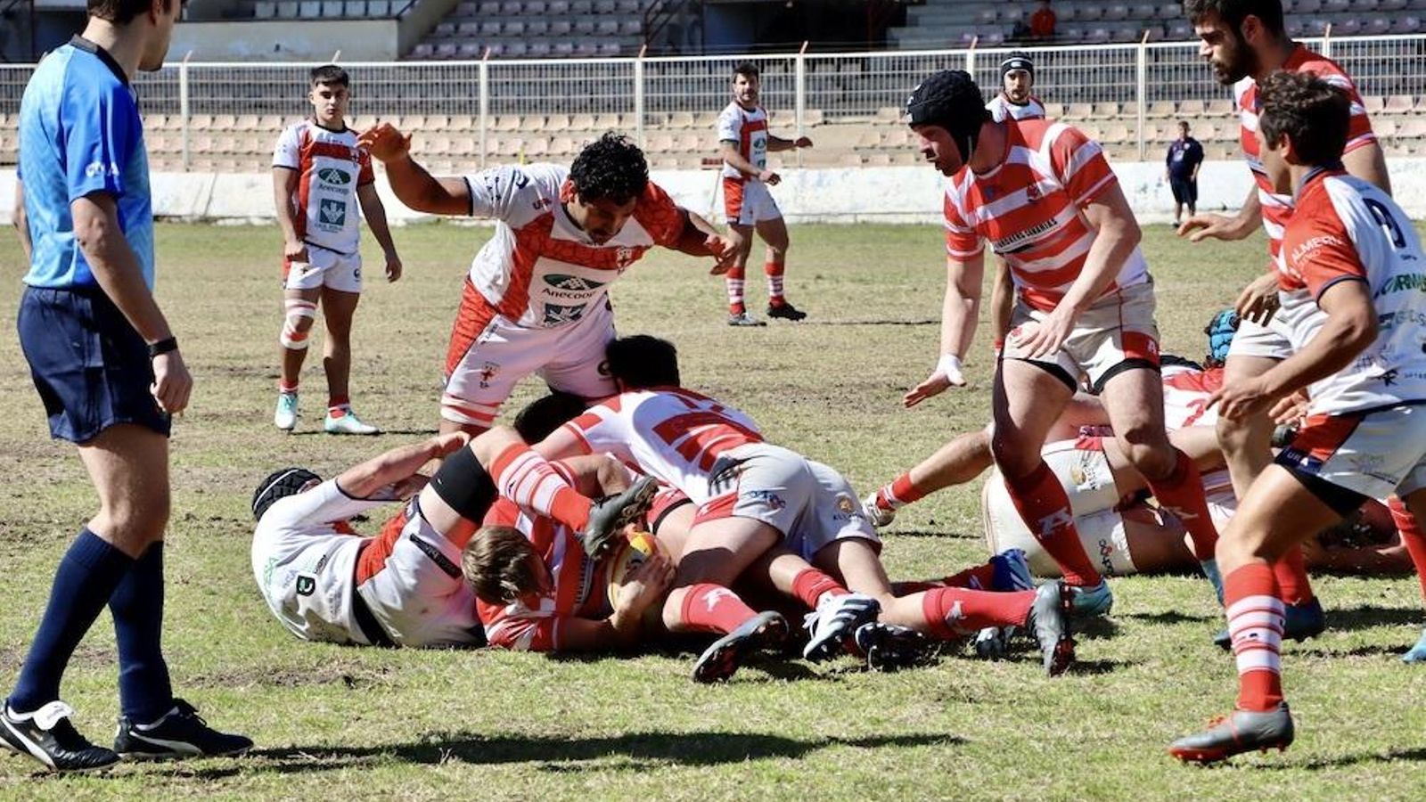 Dos jugadores cruzados intentan robar el balón a un rival que se encuentra en el suelo.