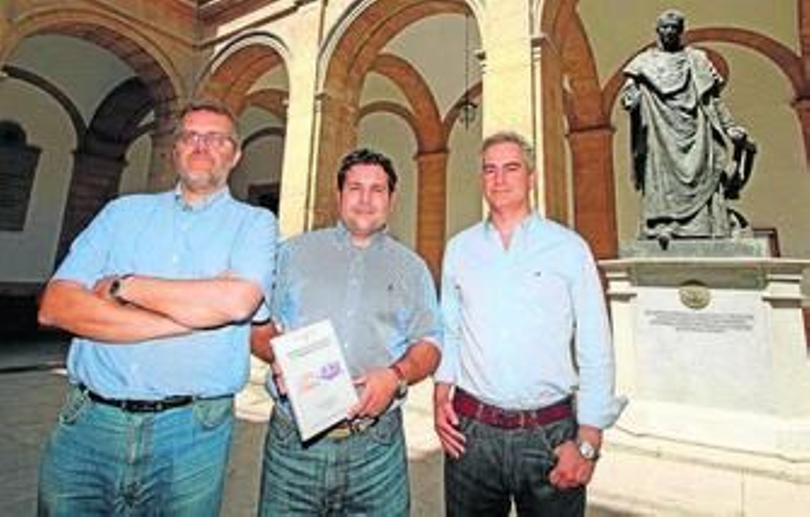 Enrique García Vargas, Alfonso Álvarez-Ossorio Rivas y Eduardo Ferrer Albelda posan con el libro delante de la estatua de Maese Rodrigo.