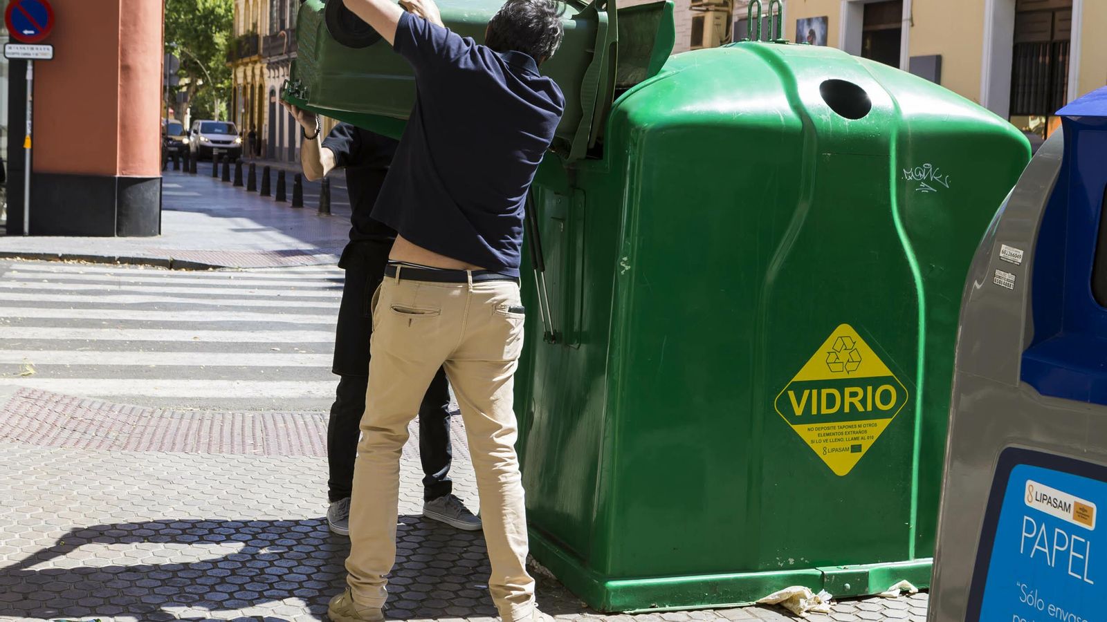 Dos personas depositan vidrio en un contenedor.