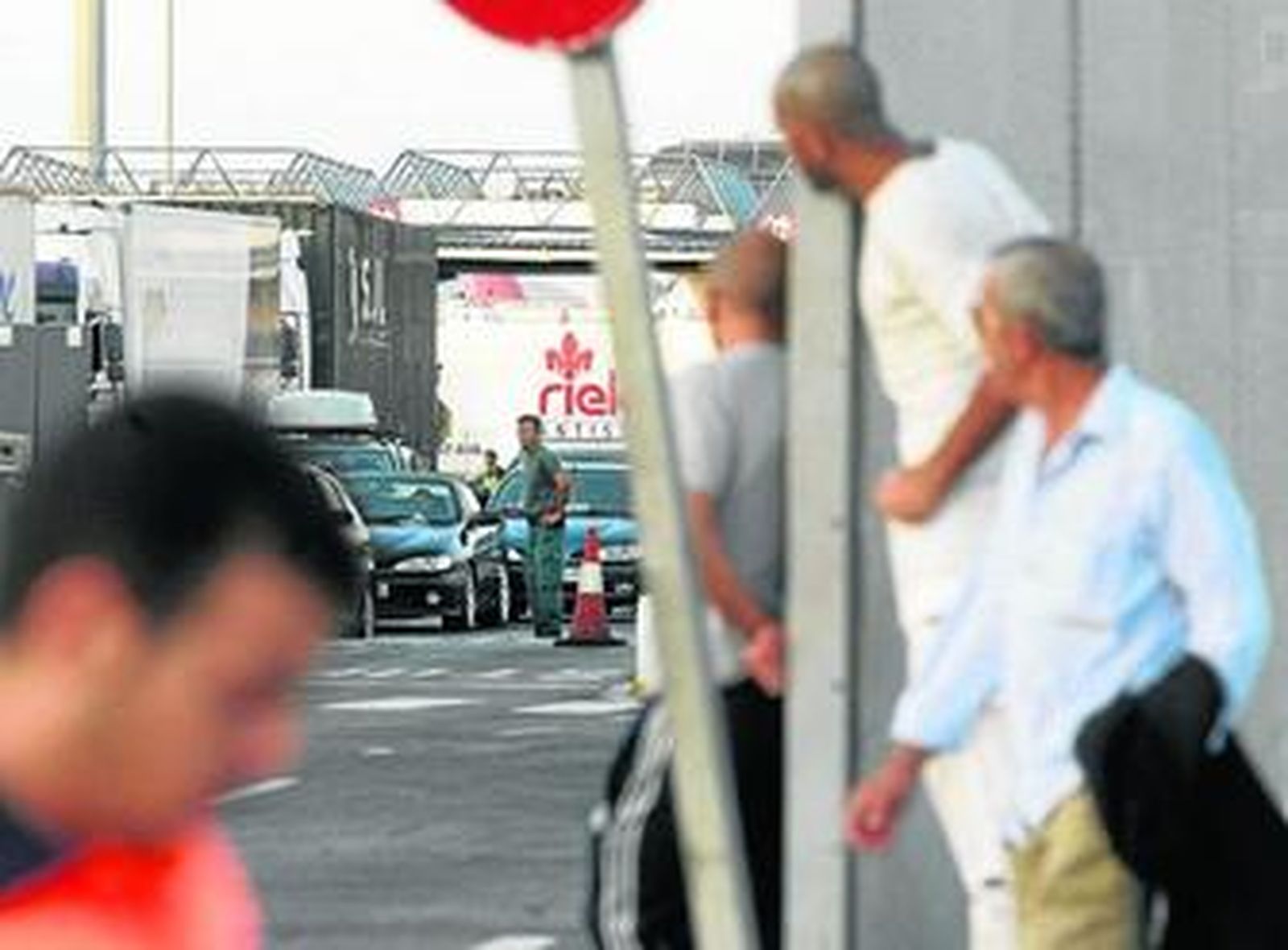 Un guardia civil controla el paso de vehículos ante la mirada atenta de unos viajeros en el puerto.