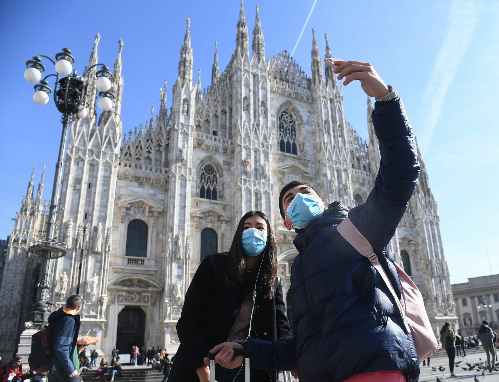Dos jóvenes se fotografían con mascarillas frente a Duomo de Milán.