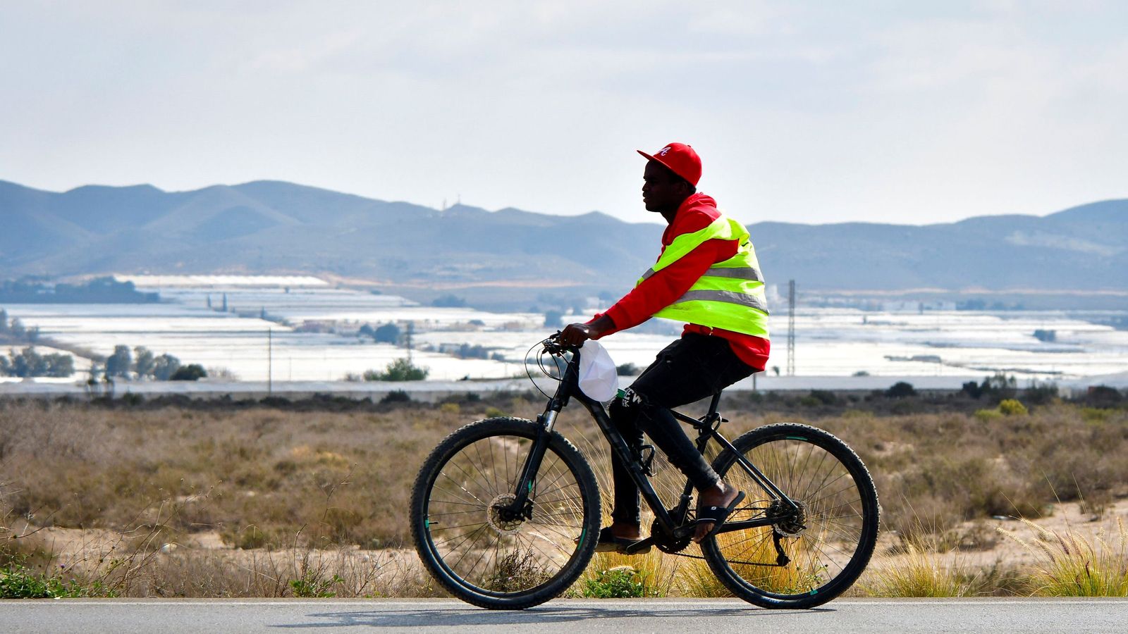 Un migrante en bicicleta en Níjar, con los invernaderos del paisaje almeriense de fondo.