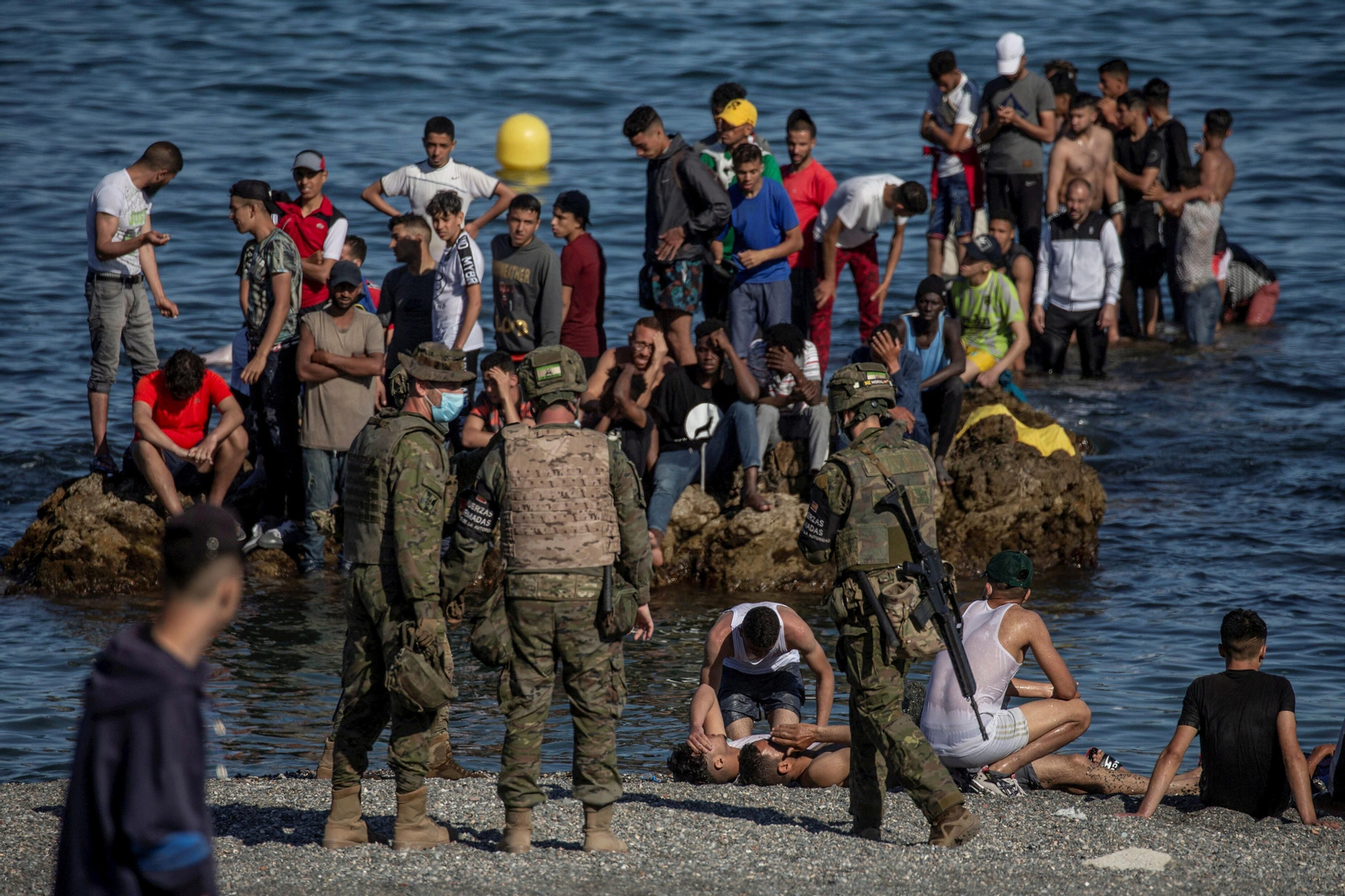 Soldados del Ejército de Tierra observan a un grupo de migrantes en la playa de El Tarajal de Ceuta.