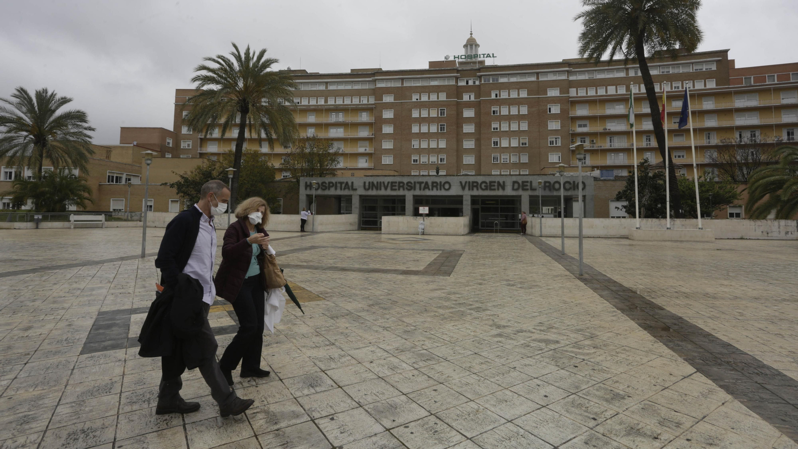 Dos personas caminan por el entorno de la entrada principal del Hospital virgen del Rocío.