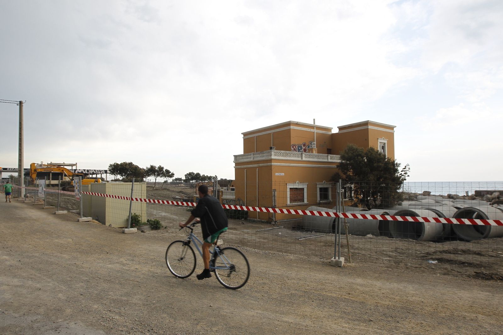 Un ciclista pasa por delante del chalet de La Marina, acordonado al encontrarse dentro del área de las obras de prolongación del paseo marítimo.