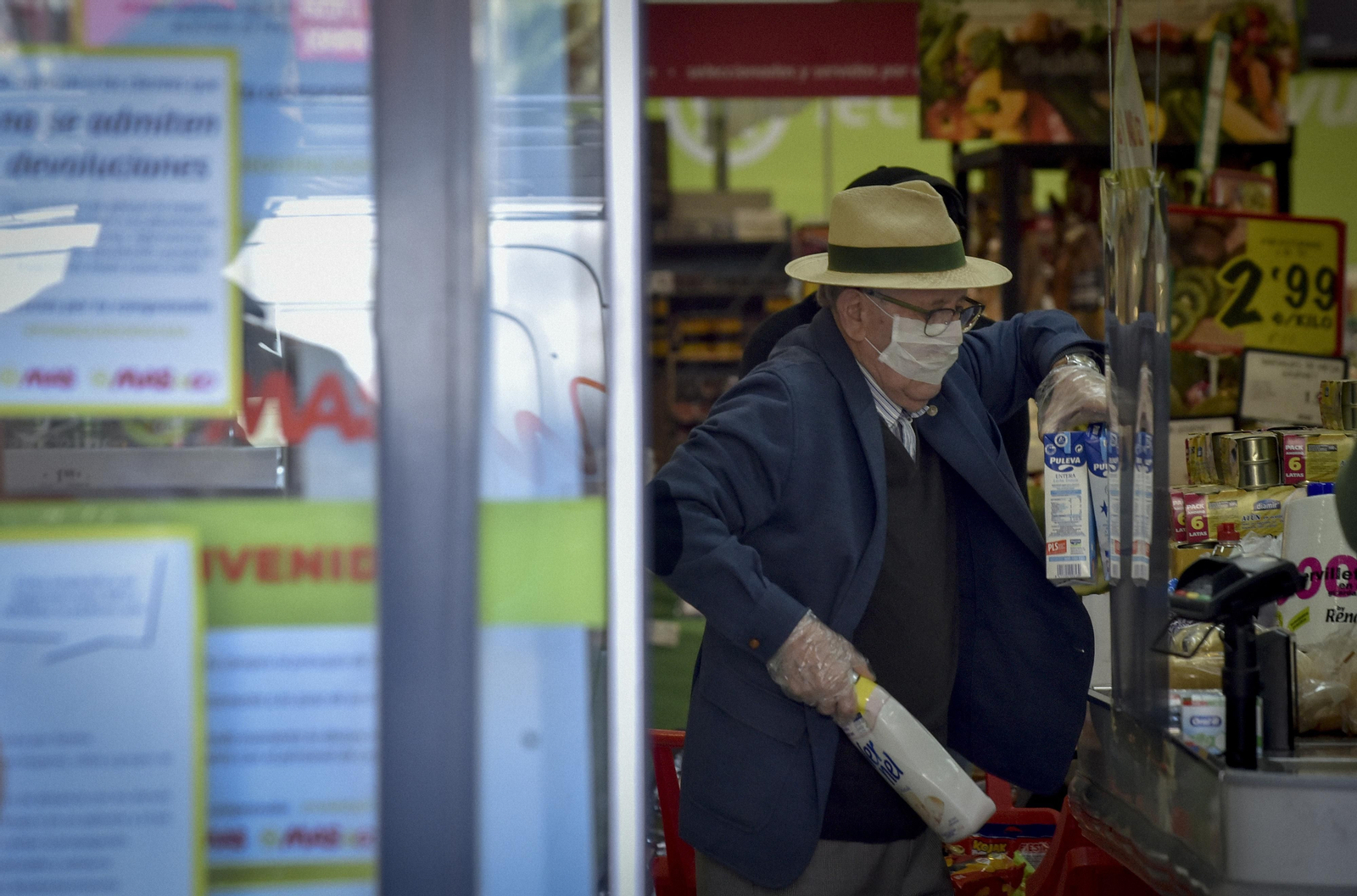 Un hombre de avanzada edad hace la compra en un supermercado con guantes y mascarilla.