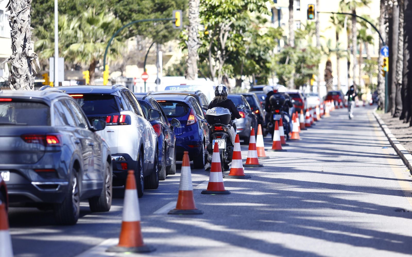 Cola de coches en el Paseo Marítimo Pablo Ruiz Picasso mientras un patinete circula por el carril 30.