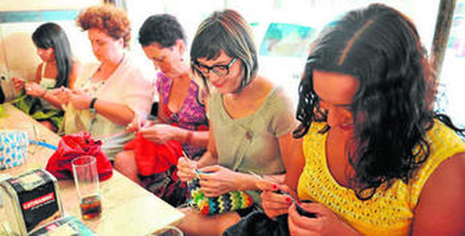 1. Integrantes del grupo de punto y crochet No8das. 2.  Una chica aprende a coger las agujas.  3. Detalle del mostrador de Devanalana junto  a un ejemplar  de la revista 'El Costurero'. 4. Una mujer prepara un ovillo de lana.  5. Beatriz, de Devanalana, inicia a una joven en el punto continental.