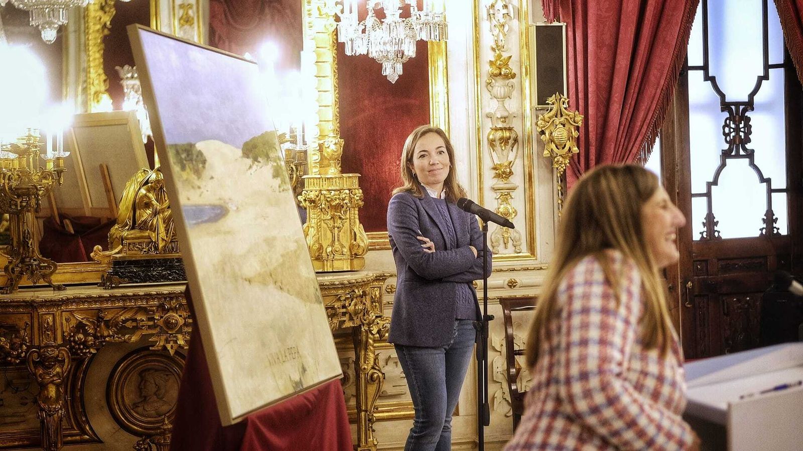 Irene García, junto a la pintura de la duna de Bolonia que anunciará la celebración y la autora de la misma, Rocío Cano.