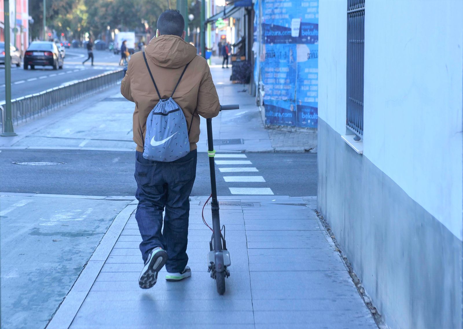 Un usuario camina con su patinete cerca del centro de la ciudad.