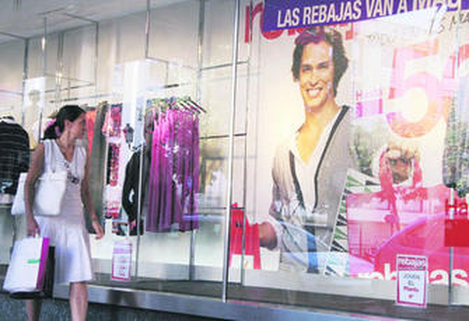 Una joven pasa junto al escaparate de El Corte Inglés presidido por el icono comercial de Carlos Baute.