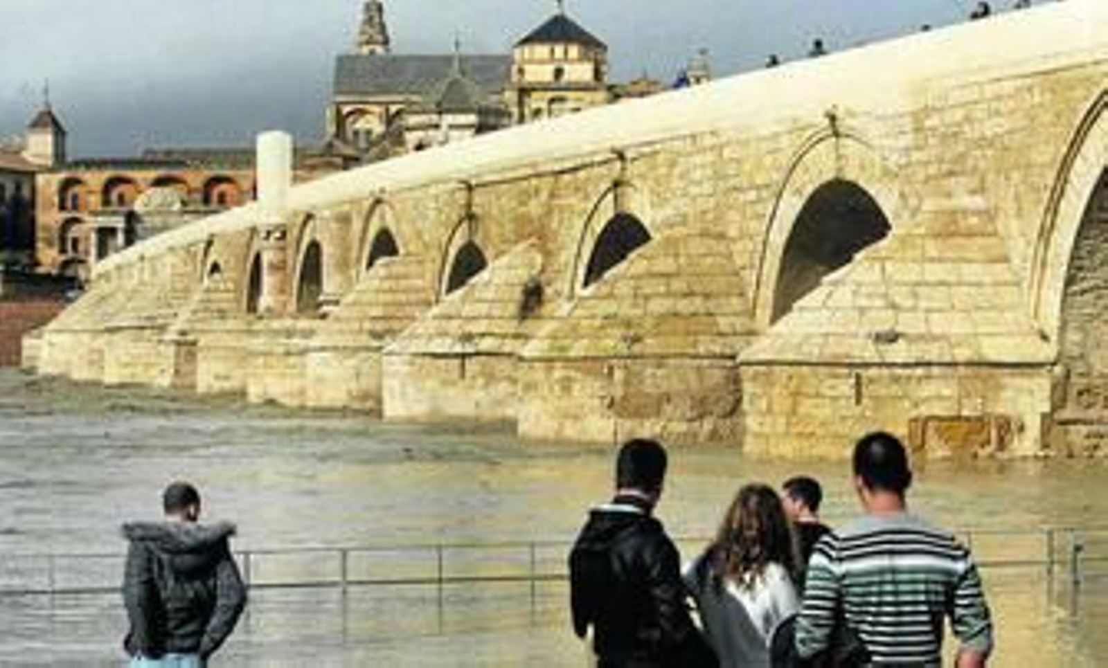Un grupo de turistas observa el Guadalquivir desde el paseo de la Calahorra, totalmente inundado.