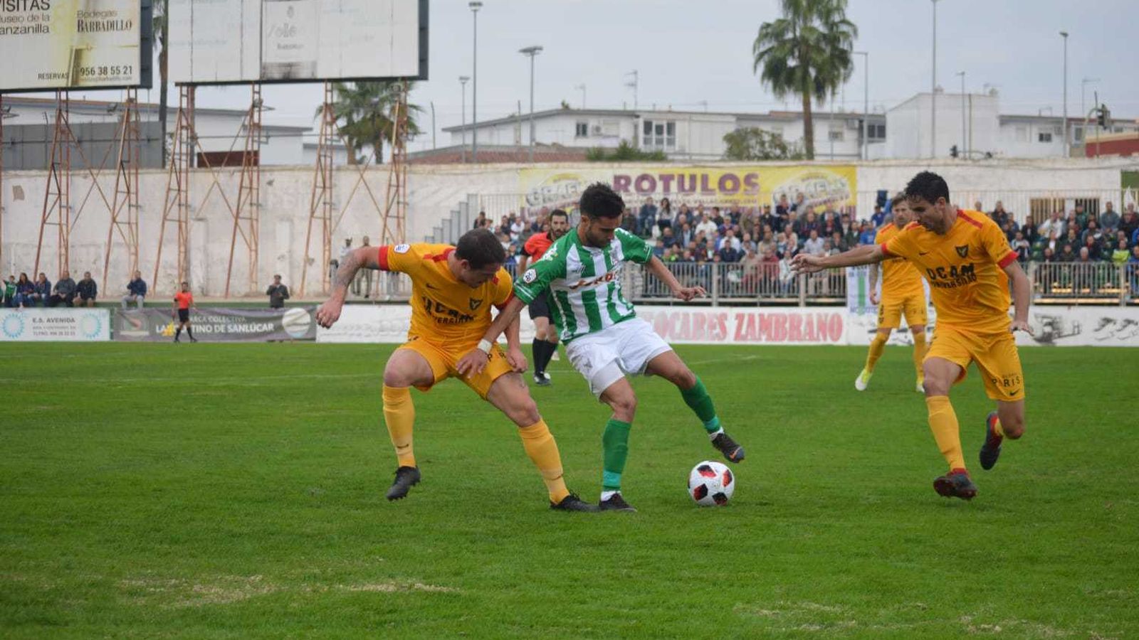 Dos jugadores visitantes, rodeando a un verdiblanco.