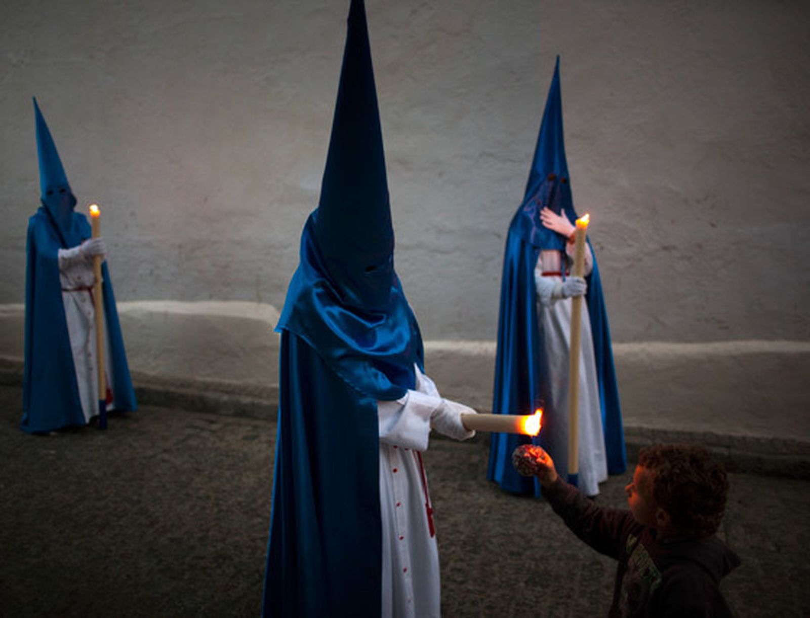 Un nazareno de la hermandad de las Viñas le da cera a un niño.  Foto: Emilio Morenatti