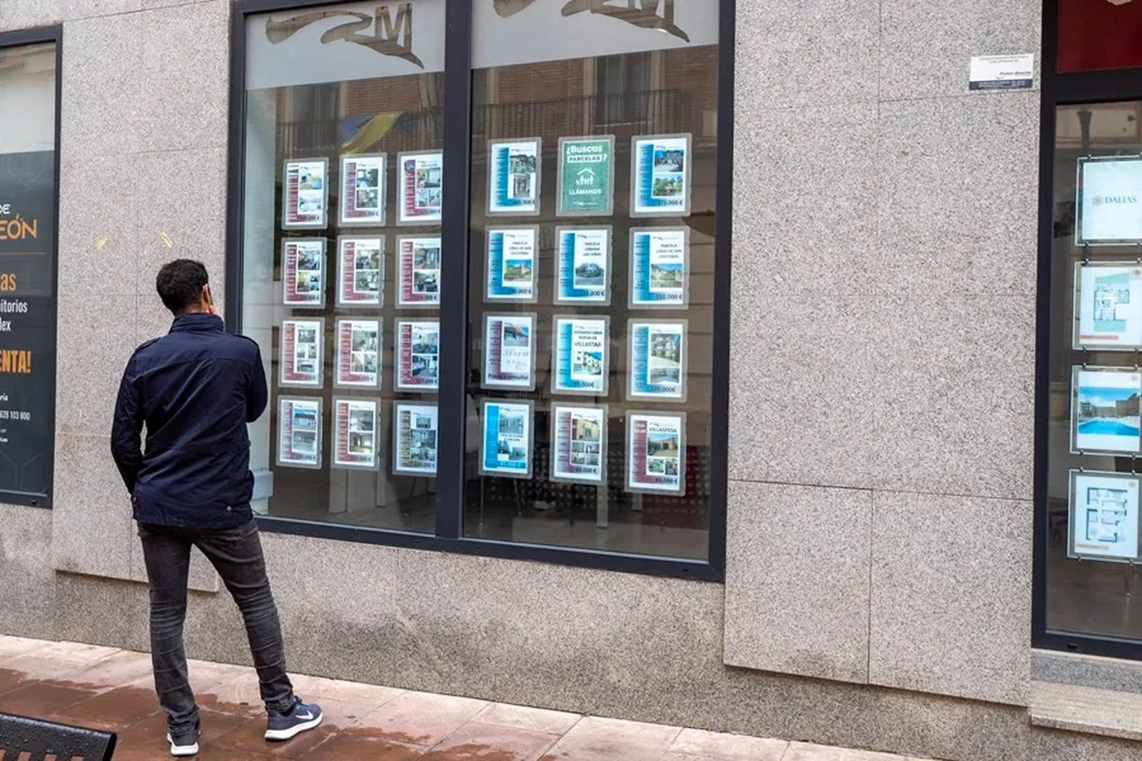 Un hombre frente a un cartel de una inmobiliaria.