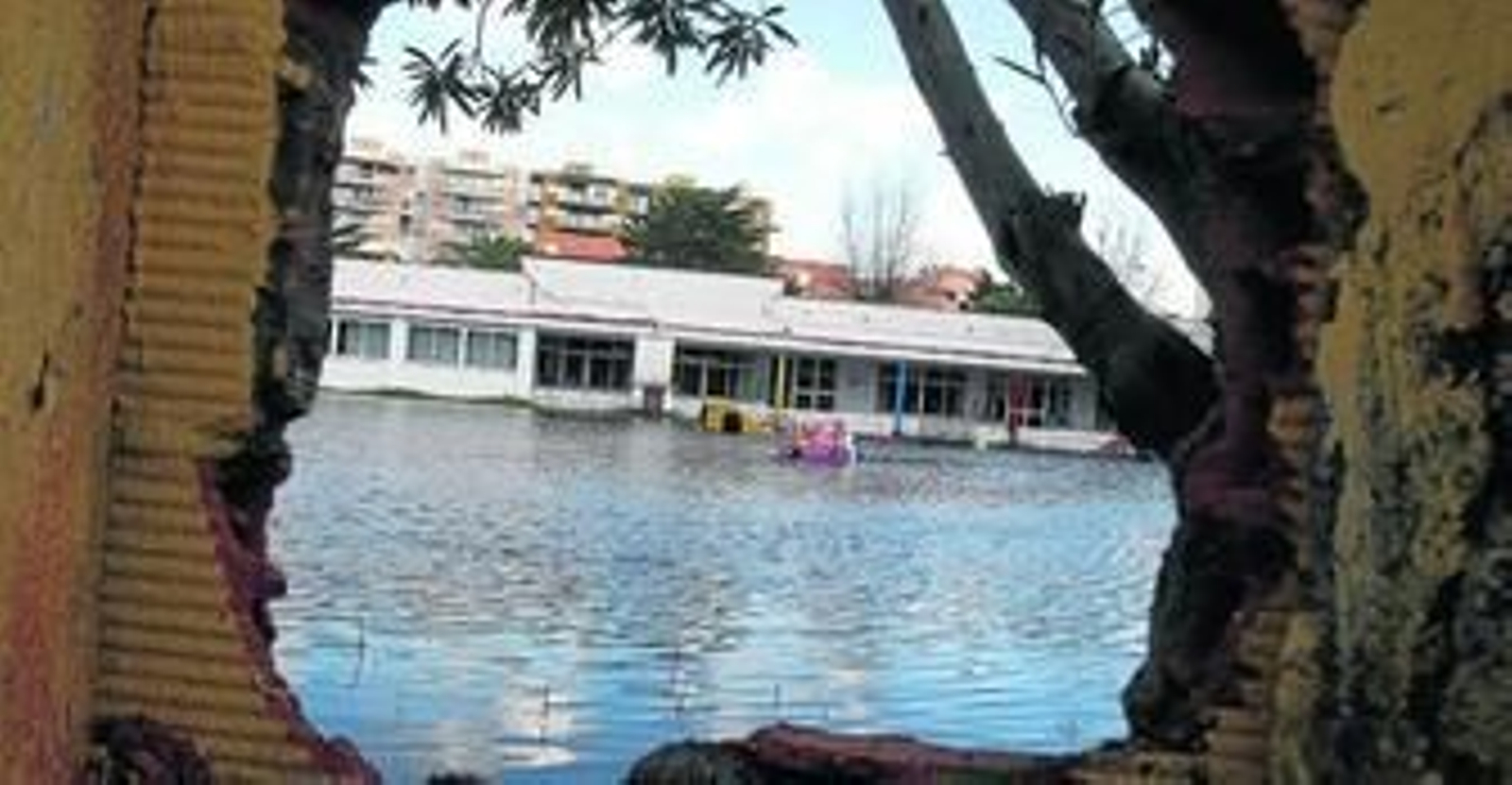 Imagen del patio de la guardería totalmente inundado, visto a través de un agujero en la tapia.