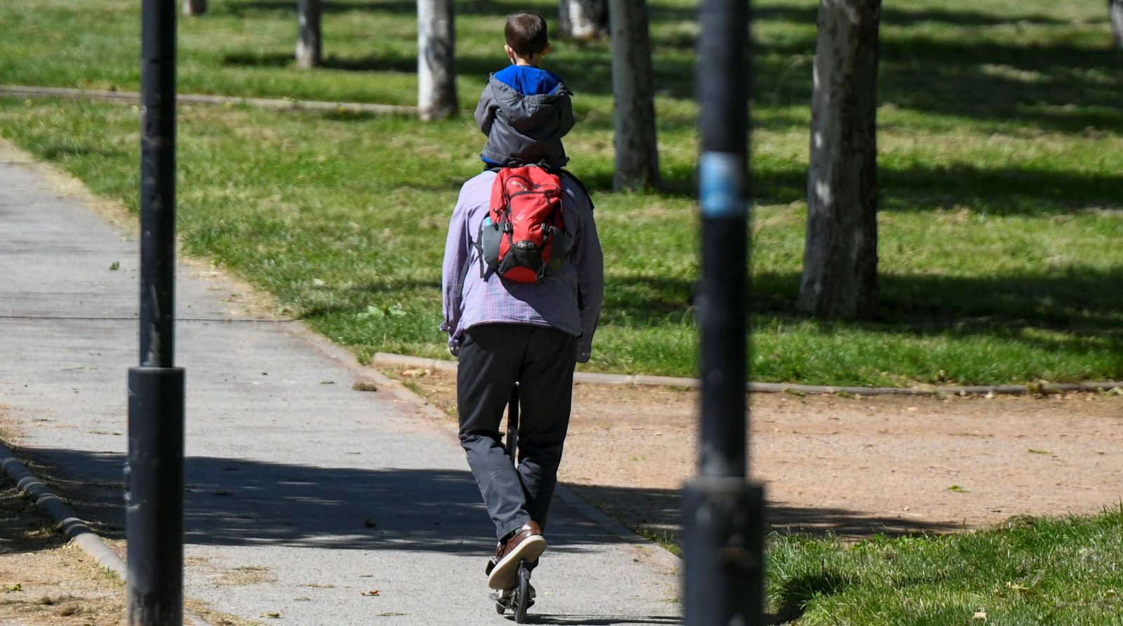 Un hombre pasea con un niño sobre un patinete.