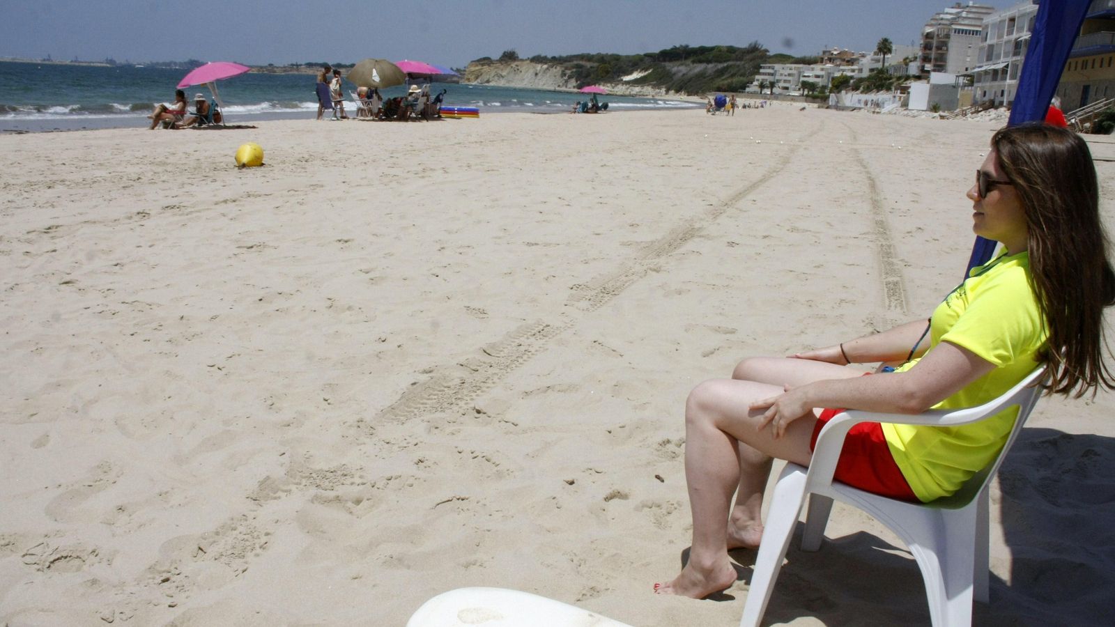 Una socorrista vigilando. Al fondo, varios grupos con sombrillas disfrutan de la playa sin bañarse.