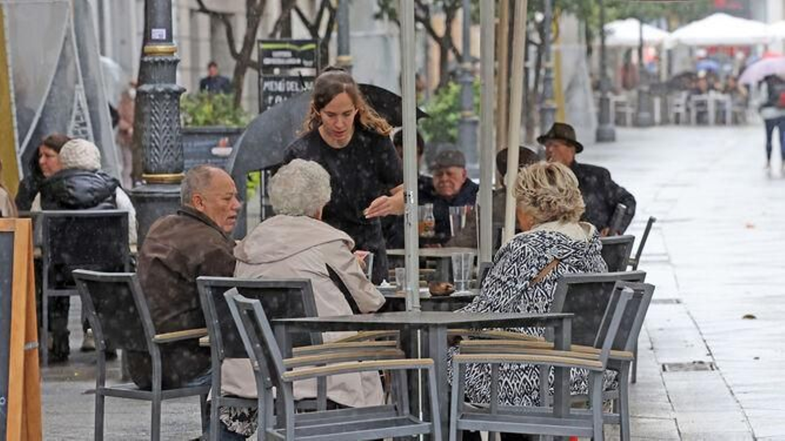 Una camarera atienda a los clientes de un bar sentados en la terraza.
