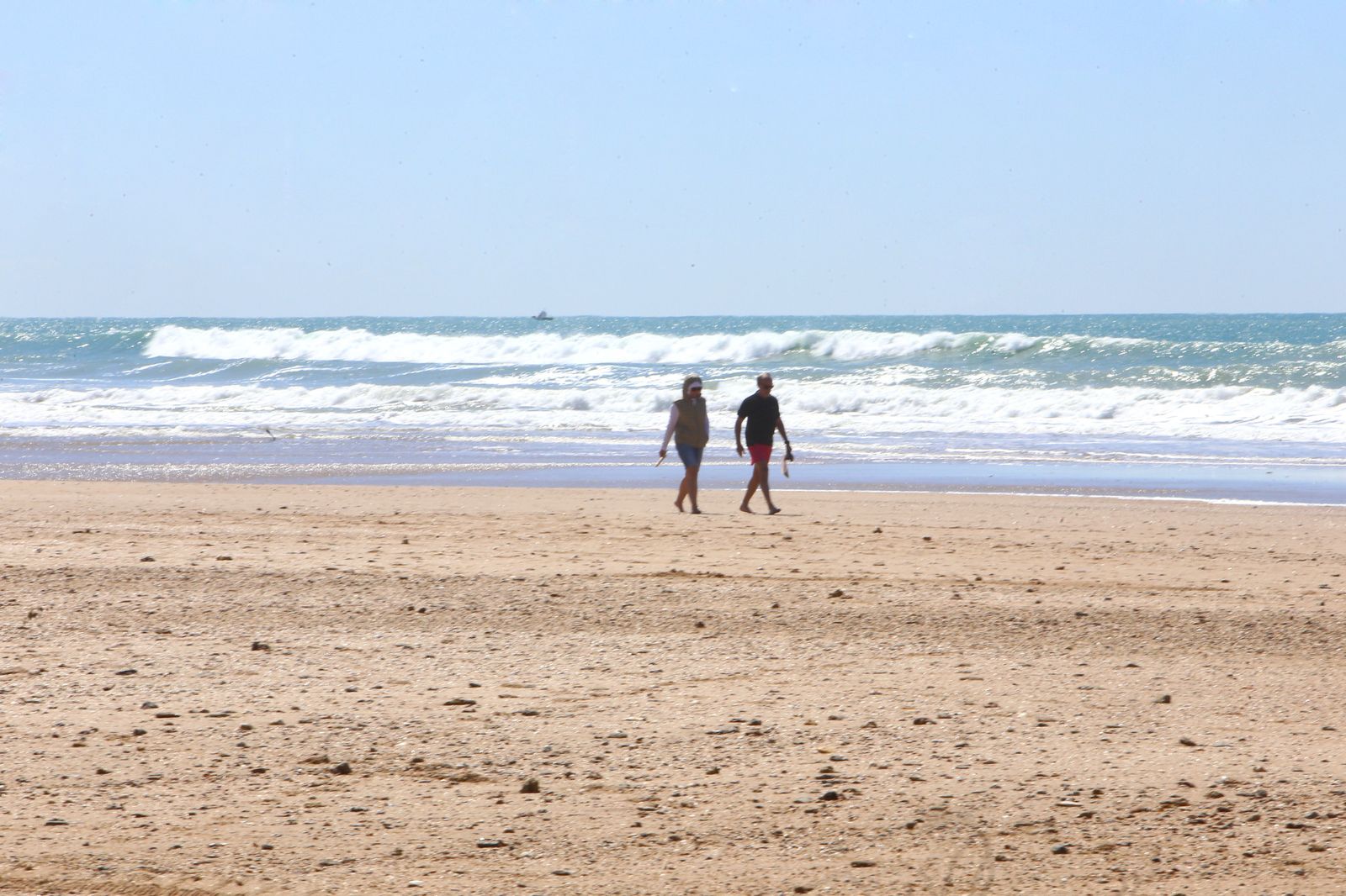 Dos personas caminan por la playa  de La Barrosa, en una imagen de archivo.