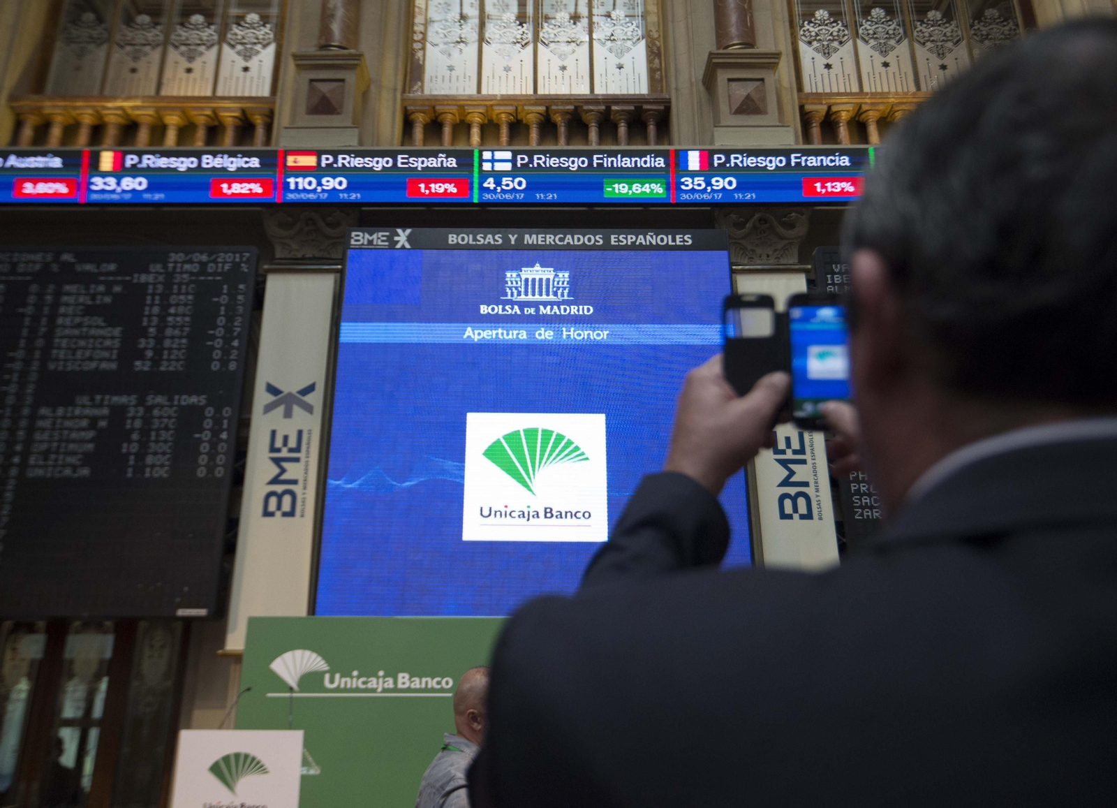 Un hombre fotografía una pantalla con los valores de Unicaja.