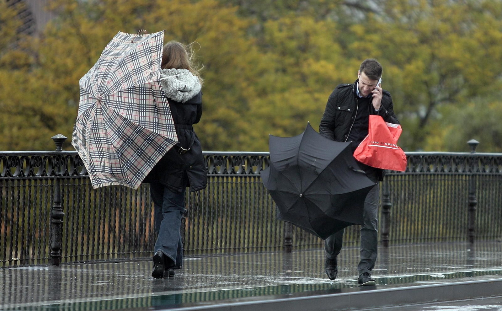 Varias personas luchan con sus paraguas contra las fuertes rachas de viento.