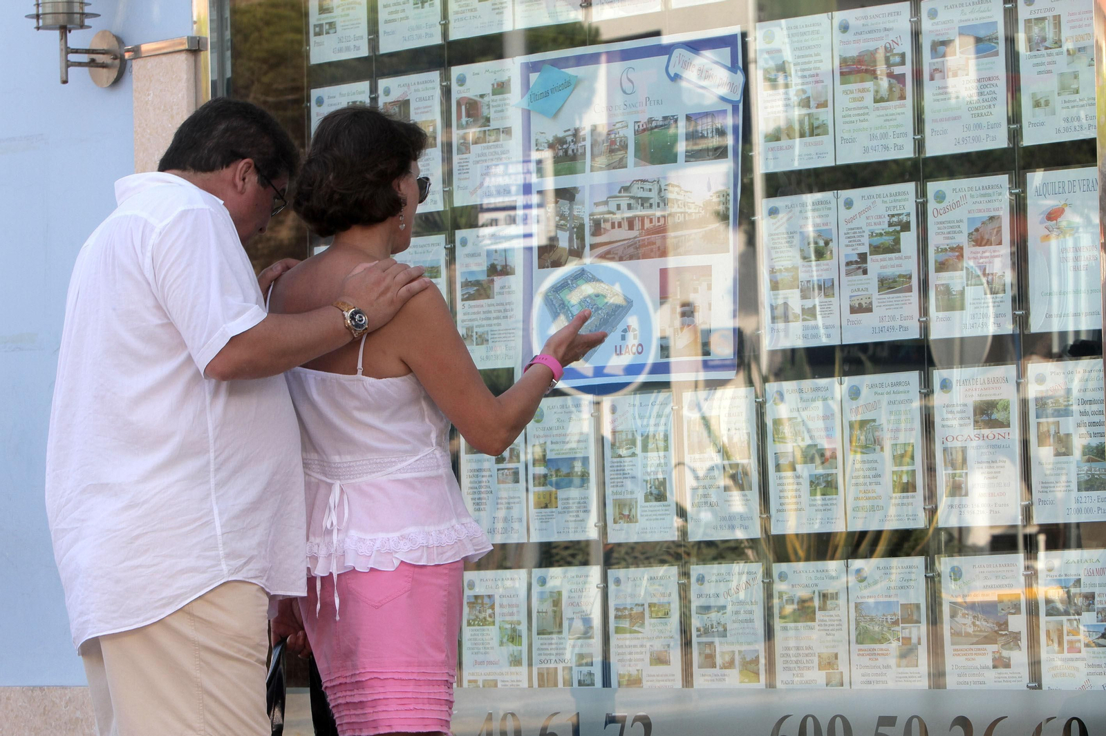 Dos personas observan el escaparate de una inmobiliaria.