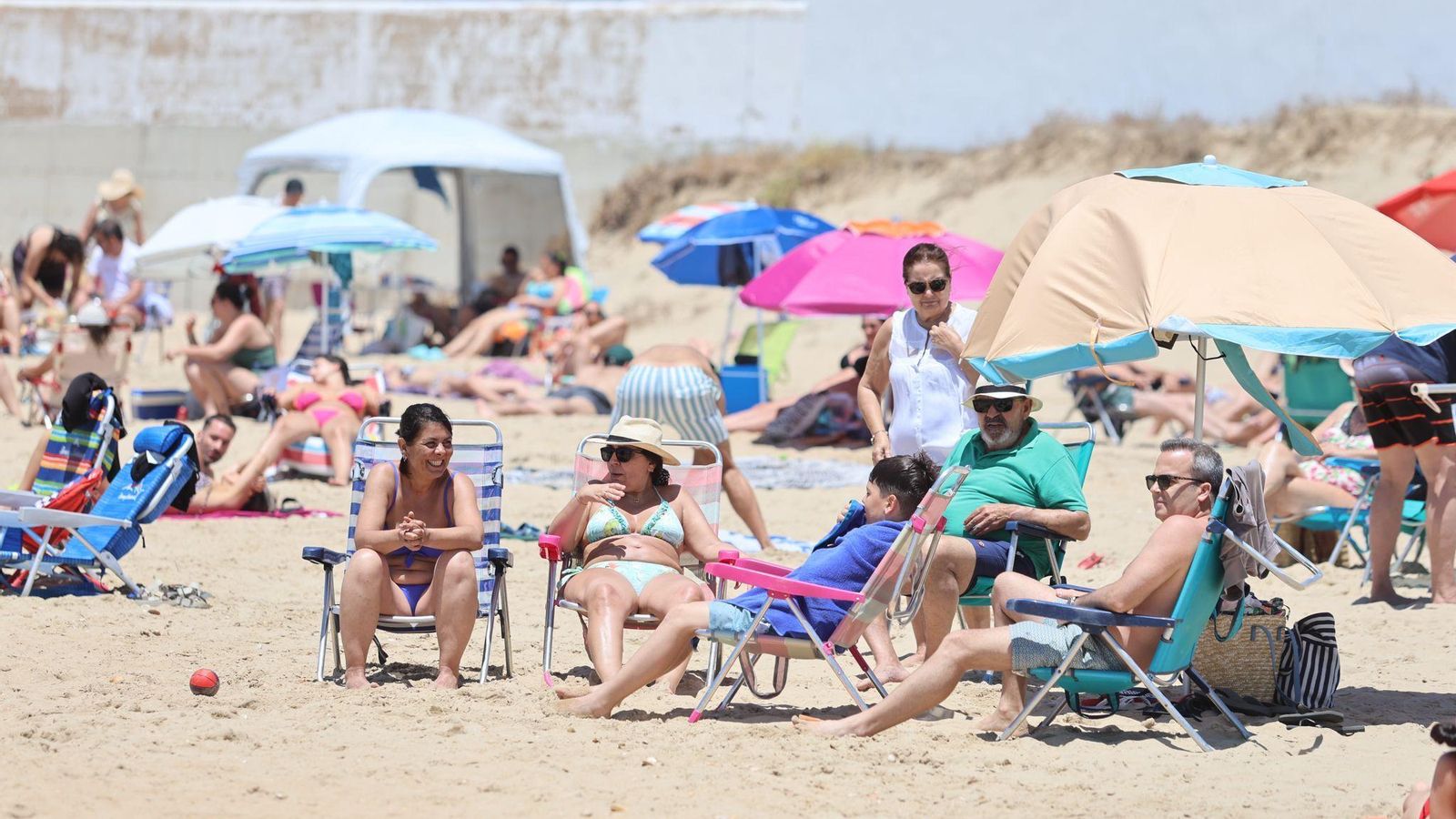 Varias personas disfrutan tomando el sol en la playa.