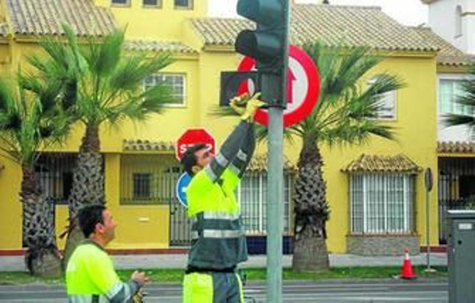 Dos operarios trabajan en la colocación de uno de los semáforos del tranvía, en la calle Feria.