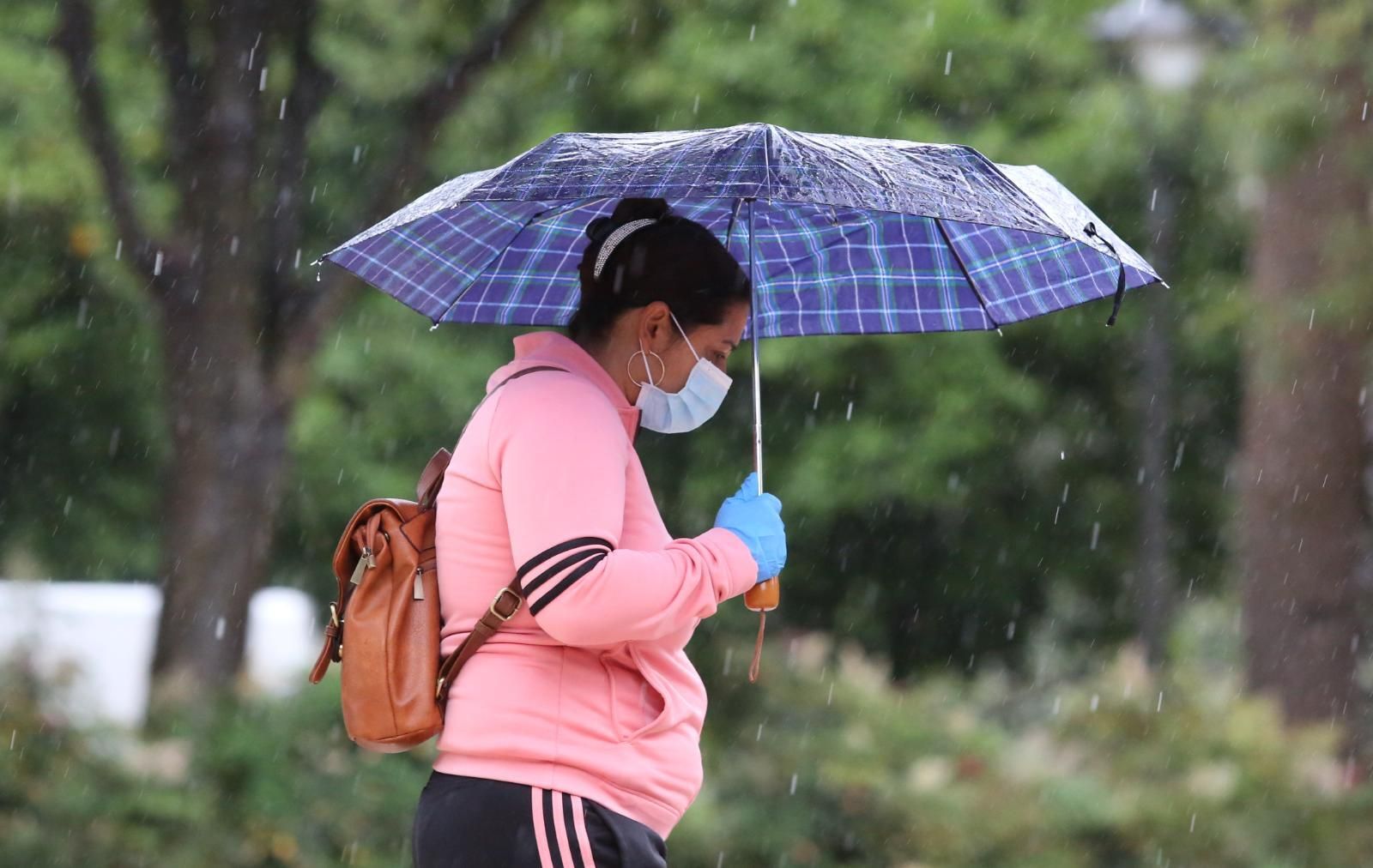 Una mujer, con mascarilla y guantes, se protege de la lluvia en Málaga capital.