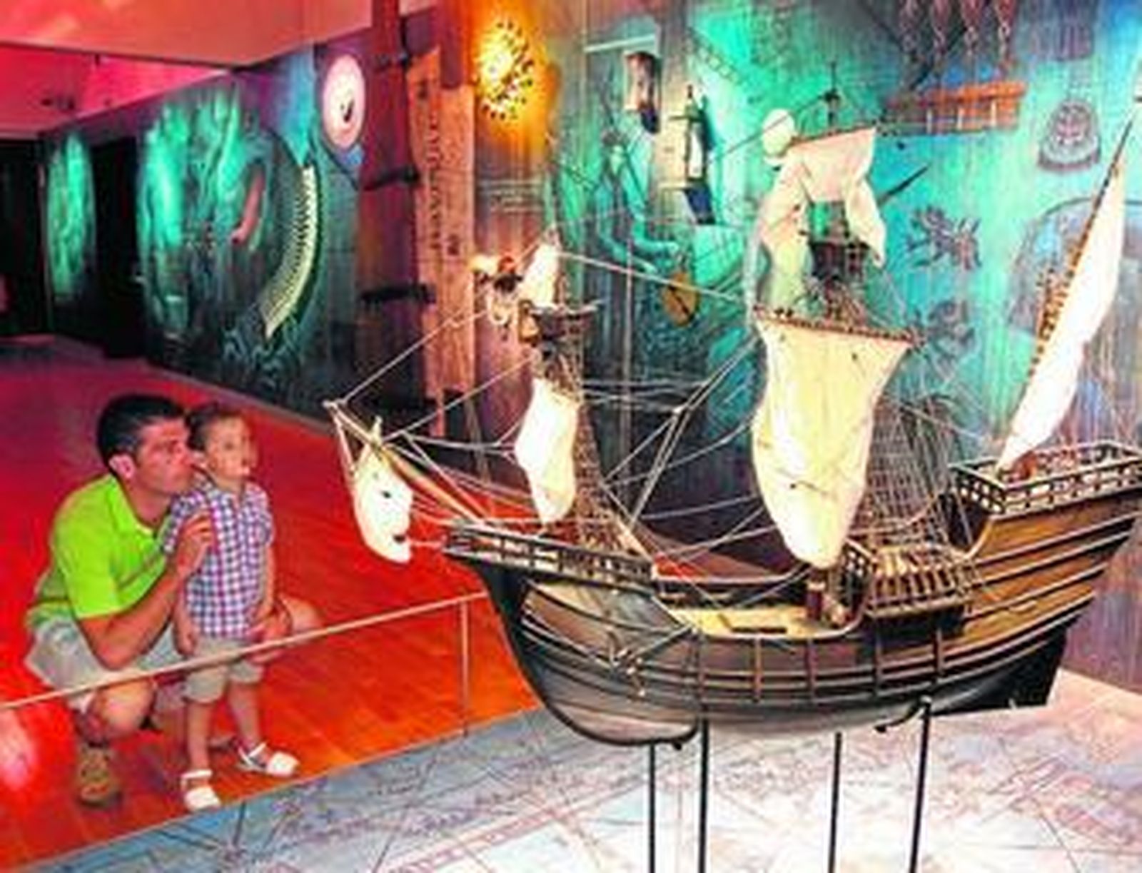 1. Un padre y su hijo observan una de las maquetas que se encuentran dentro del Pabellón de la Navegación. 2. El personaje de Lola Chacón, tabernera del siglo XVI, cuenta anécdotas de la época a los visitantes durante el recorrido. 3. La vista panorámica del Pabellón de la Navegación iluminado es la primera de las paradas de este viaje.